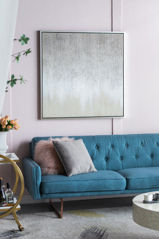 A modern living room with a blue tufted sofa, pink and gray cushions, a round coffee table, gold bar cart, vase of flowers, and the Sunshine Framed Hand Painted Canvas Print Wall Art on a pale pink wall.