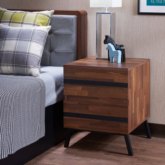 A modern bedroom features the Karine Accent Table in black/walnut, topped with a clear lamp and two horse figurines. A gray-upholstered bed is styled with striped and plaid pillows plus a gray blanket.