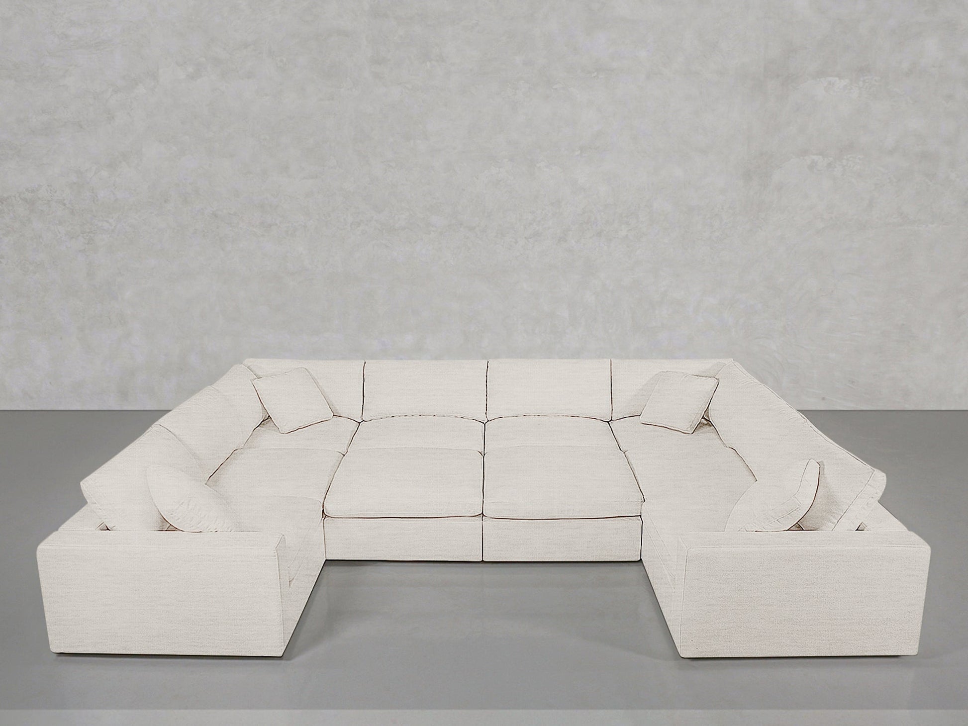 The 10-Seat Modular Closed Pit is a large, modern U-shaped sectional in light beige fabric with six matching square cushions, set against a plain light gray wall and floor.