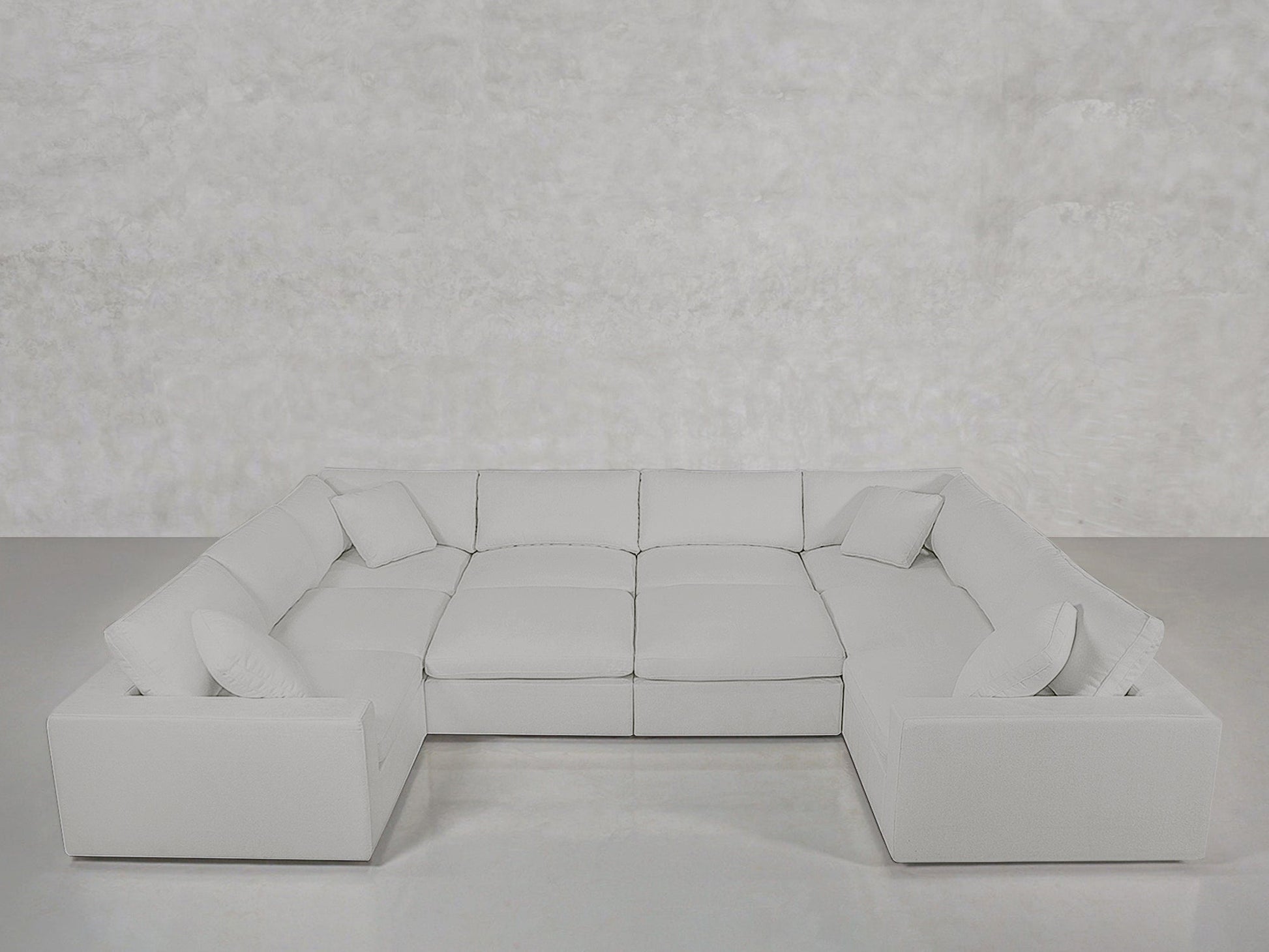 The 10-Seat Modular Closed Pit is a large, light gray U-shaped sectional with six seat cushions and four throw pillows, set against a minimal light gray wall and floor.