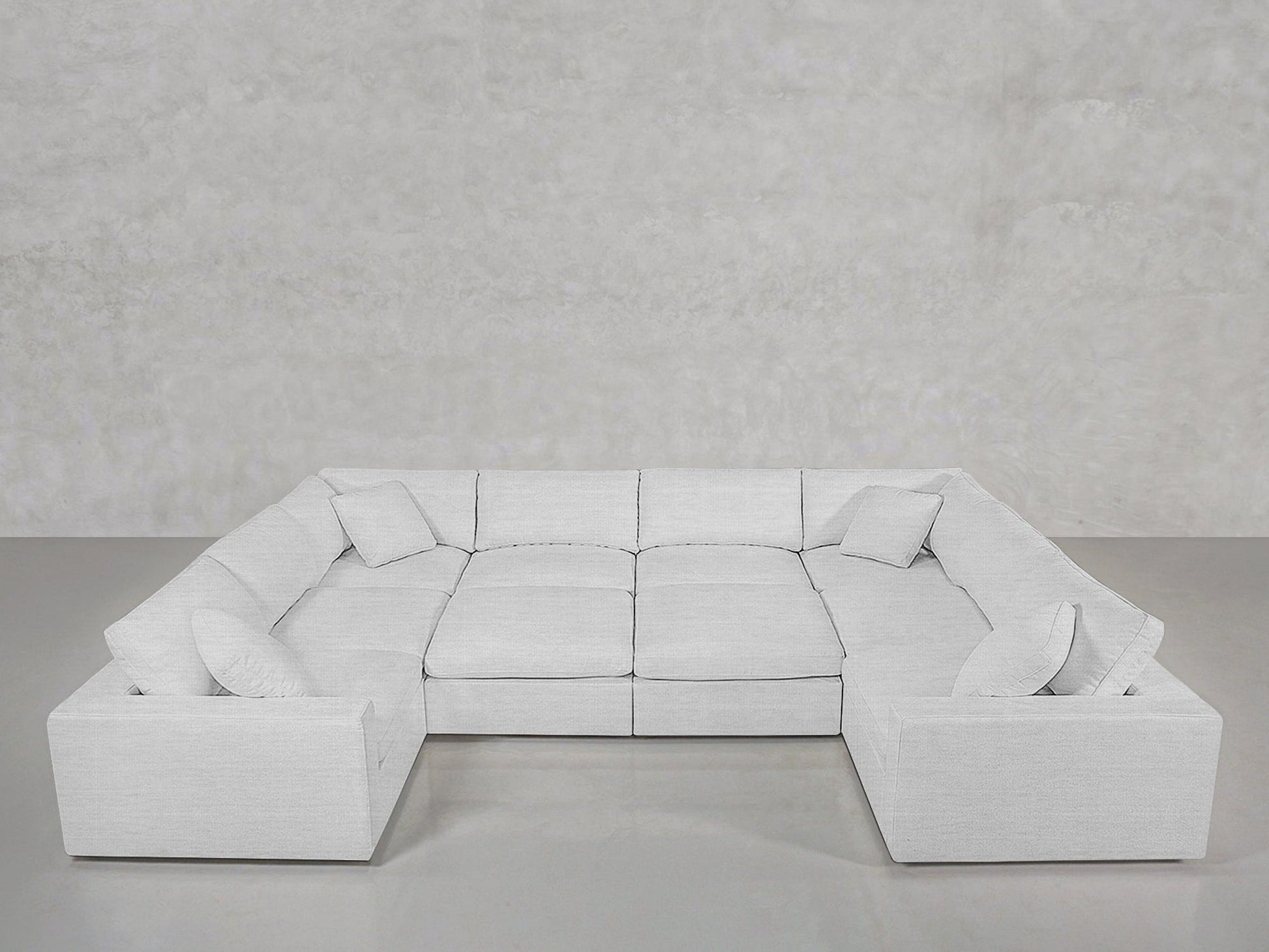 A spacious, modern 10-Seat Modular Closed Pit in light gray with six seat cushions and five matching throw pillows, arranged in a U-shape against a plain, light gray wall and floor.