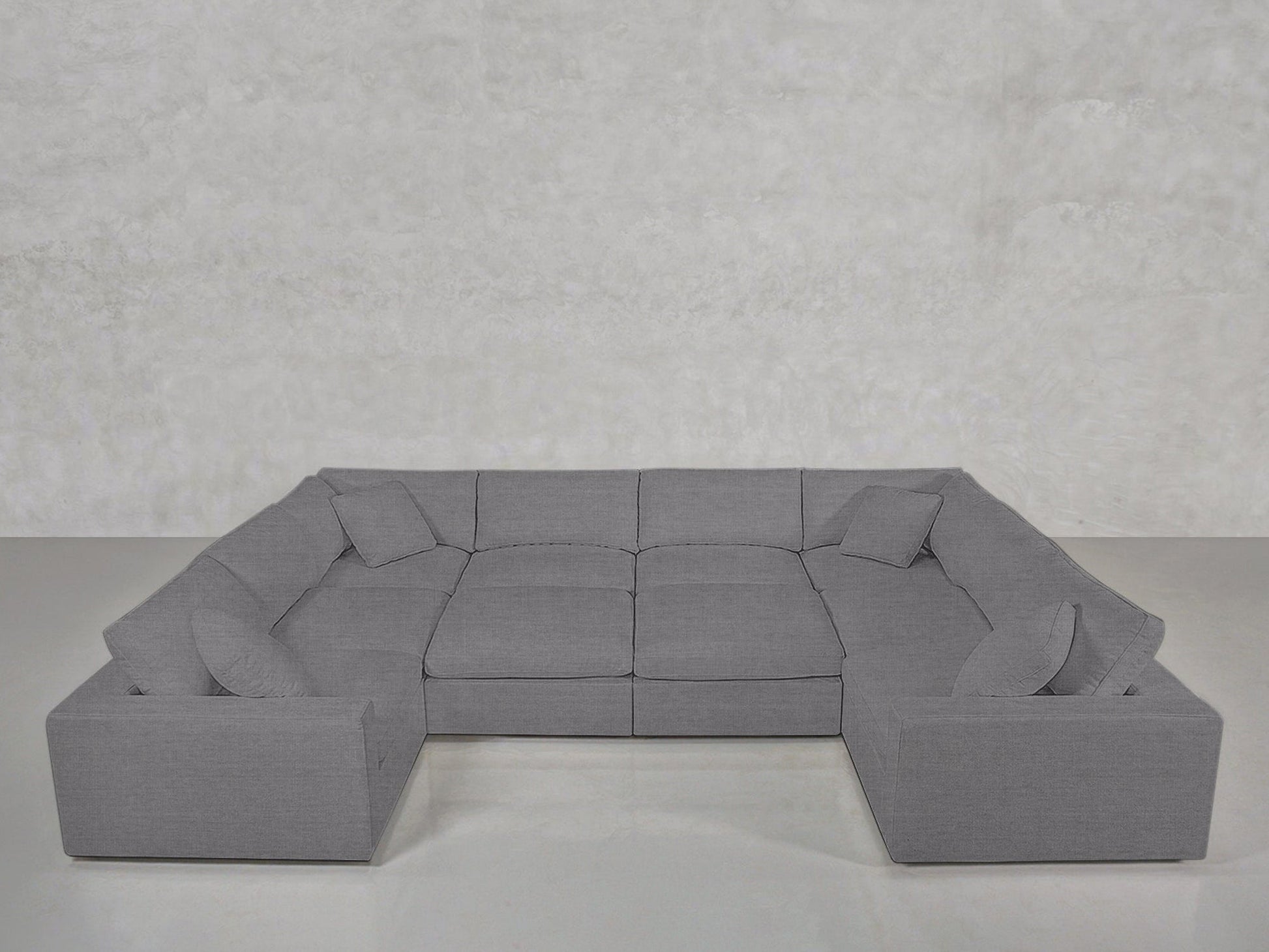 A modern light gray 10-Seat Modular Closed Pit sectional with six seat cushions and five matching throw pillows sits against a plain light gray textured wall on a light floor.