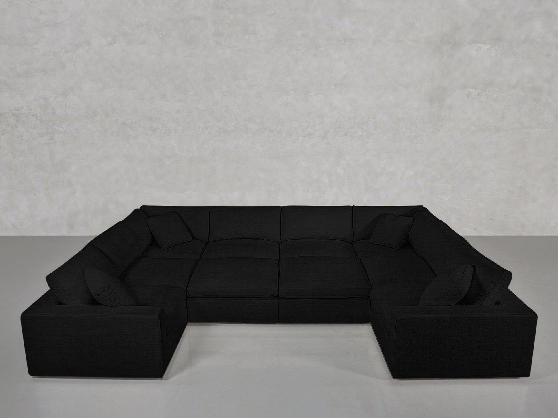 A spacious, modern black 10-Seat Modular Closed Pit sectional with clean lines and low backrests, arranged in a U-shape against a light gray textured wall, includes four matching black cushions.