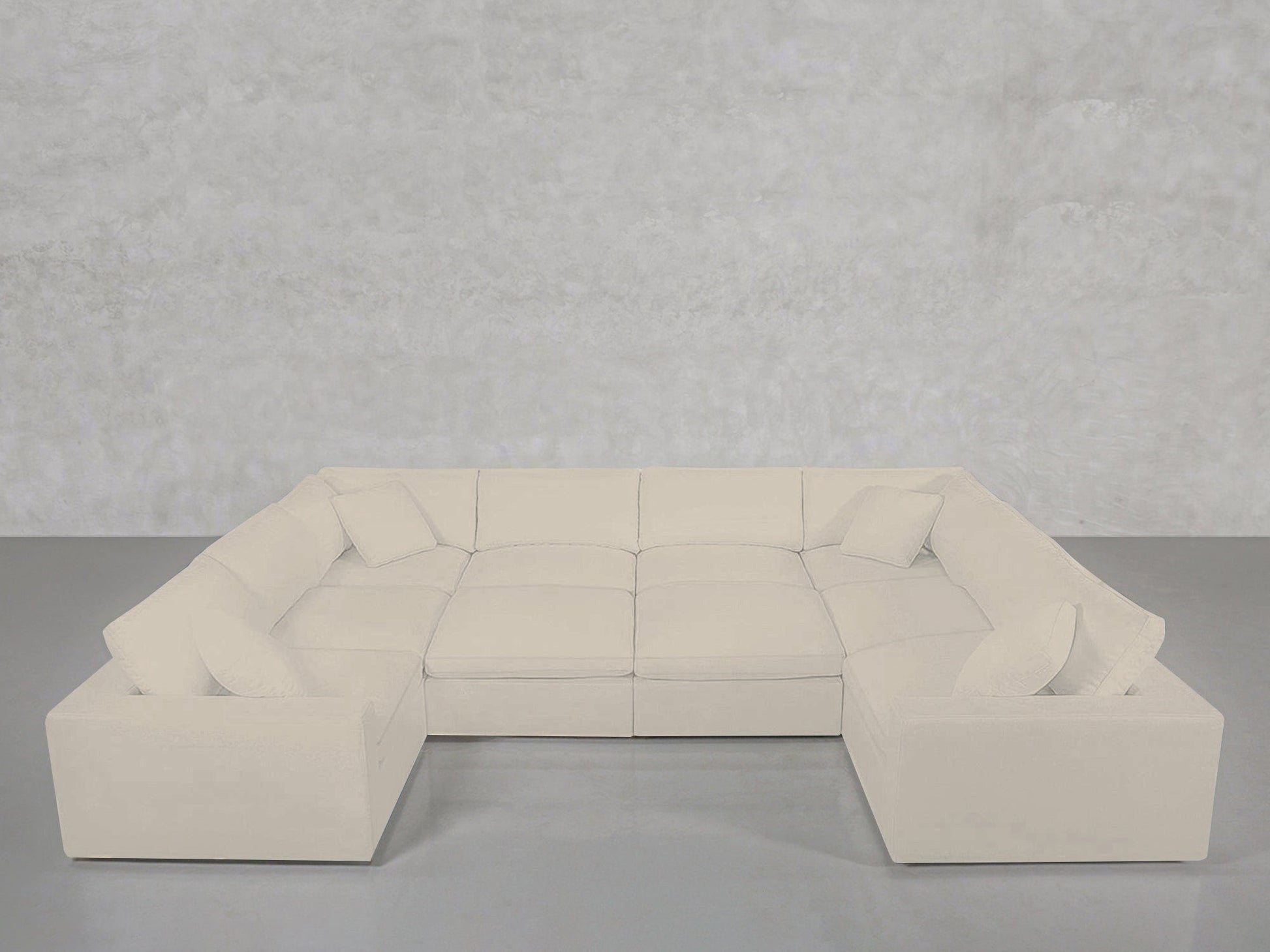 A spacious, light cream 10-Seat Modular Closed Pit sectional with plush cushions and matching throw pillows, arranged against a plain light grey wall and floor.