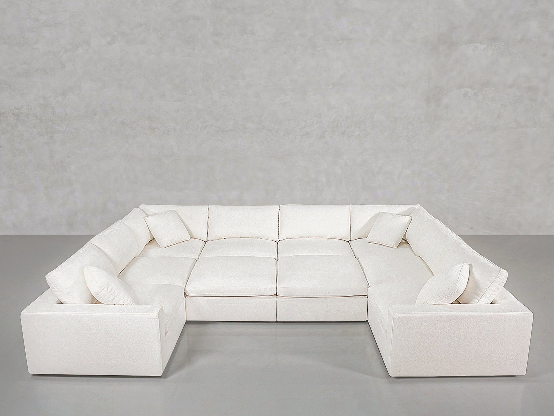 Spacious 10-Seat Modular Closed Pit sectional sofa in modern white, featuring six seat cushions and four matching throw pillows, placed before a plain light gray wall and smooth gray floor.