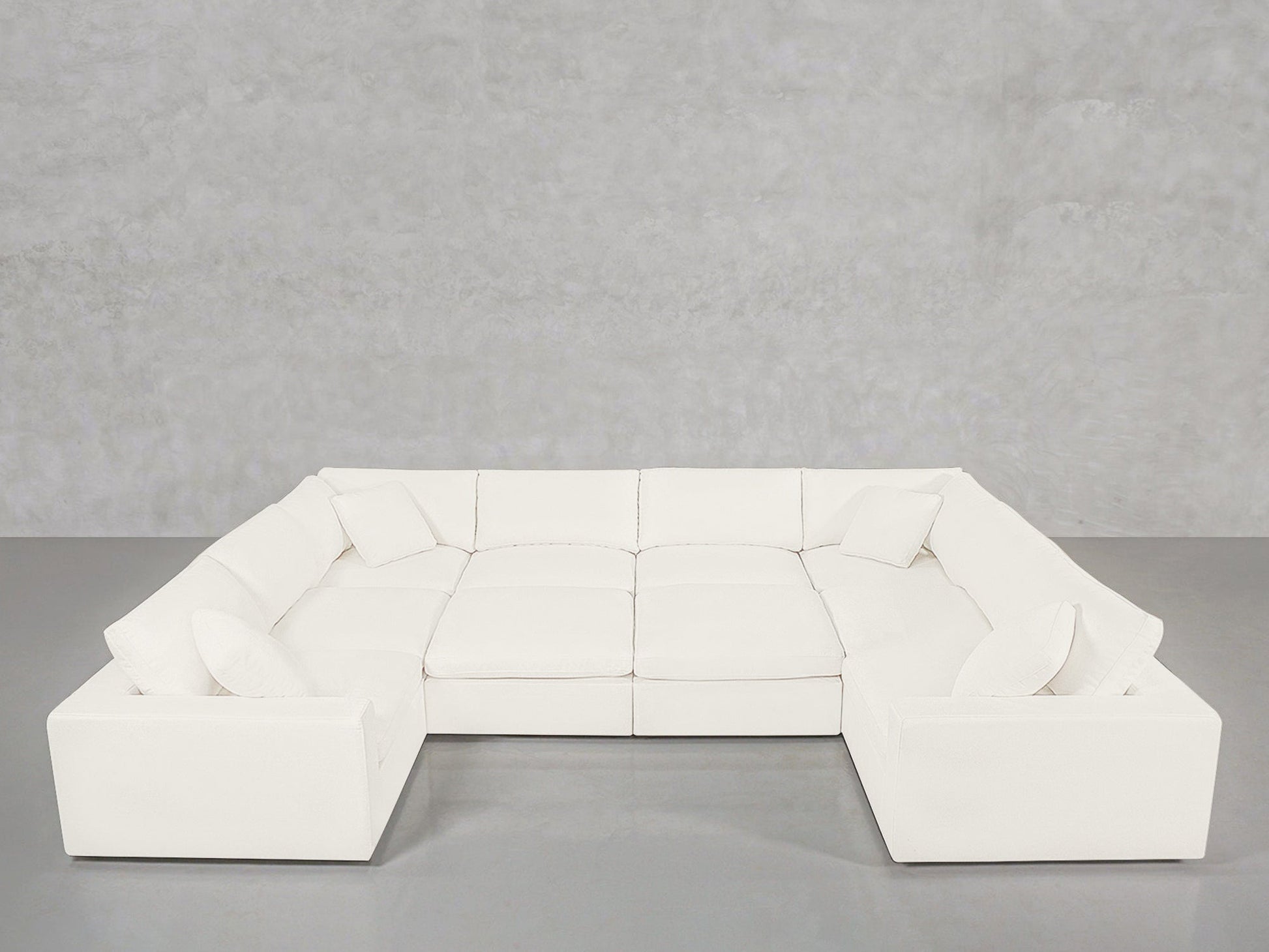 A spacious, white 10-Seat Modular Closed Pit sectional with matching cushions sits against a plain light gray concrete wall and floor.