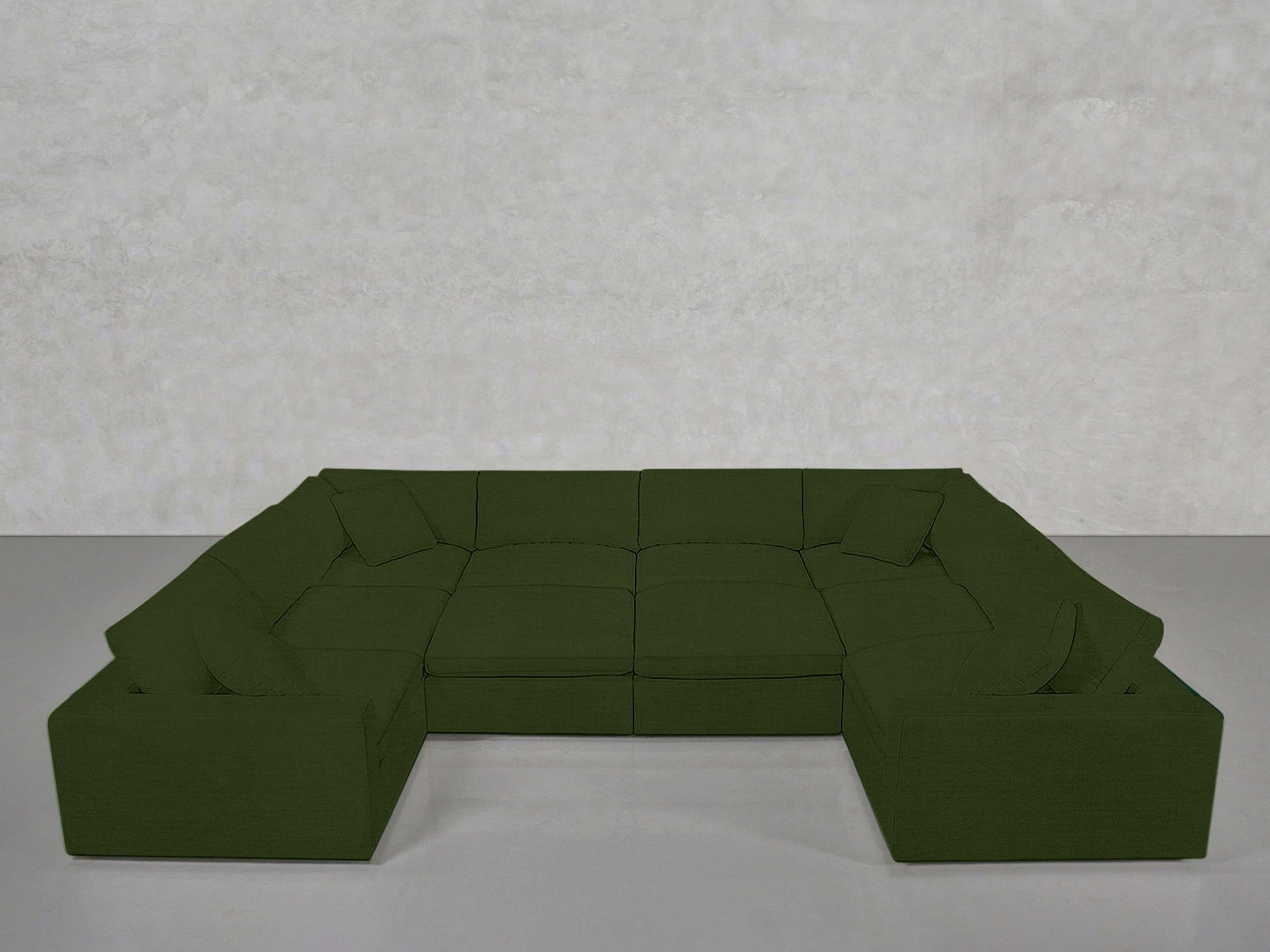 A modern 10-Seat Modular Closed Pit in dark green, featuring wide seats and low backrests, is arranged in a U-shape against a light gray textured wall in a minimalist room.