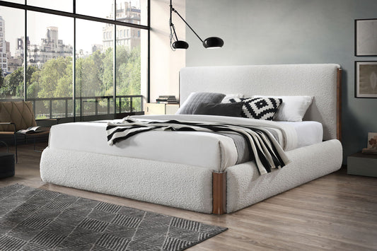 Modern bedroom with the Sandro Eastern King Bed Boucle in Walnut/White, black and white patterned pillows, a striped blanket, floor-to-ceiling windows showing city views and trees, plus a geometric rug on the wooden floor.