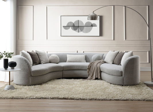 A modern living room featuring the Ivria Boucle Sectional Sofa with 9 pillows in gray, neutral throw pillows, a beige rug, a round side table with decor, a floor lamp, and minimalist black and white abstract wall art.