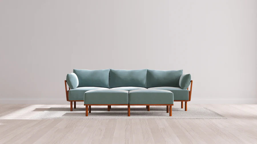 In a bright and airy minimalist living room featuring a light wooden floor and plain walls, the Indoor Jack 3-Seater Sofa + Bench Ottoman in Balsa adds a modern touch, placed on a light-colored rug.