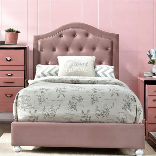 A neatly made Reggie Twin Bed in pink with a tufted velvet headboard, floral bedding, decorative pillows (one says "Home Sweet Home"), and two pink nightstands against a pink paneled wall.