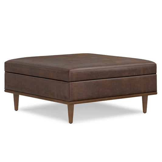The Shiloh Multifunctional Square Storage Ottoman features brown leather upholstery, a cushioned top, and four tapered wooden legs, shown against a white background.