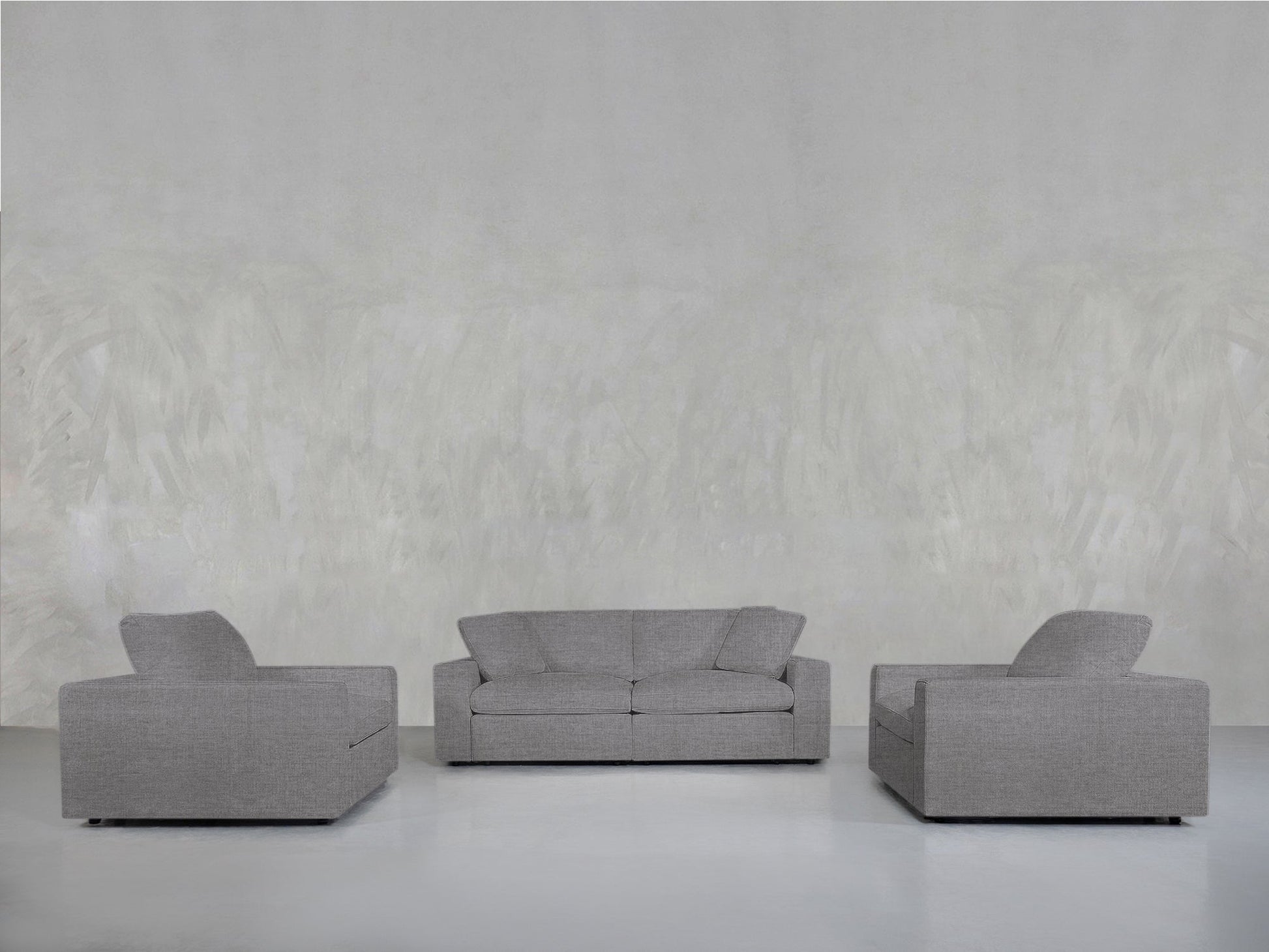 A 2-1-1 Sofa & Armchair Set in modern gray upholstery is arranged in a U-shape against a plain light gray textured wall in a spacious, minimalistic room with a white floor.