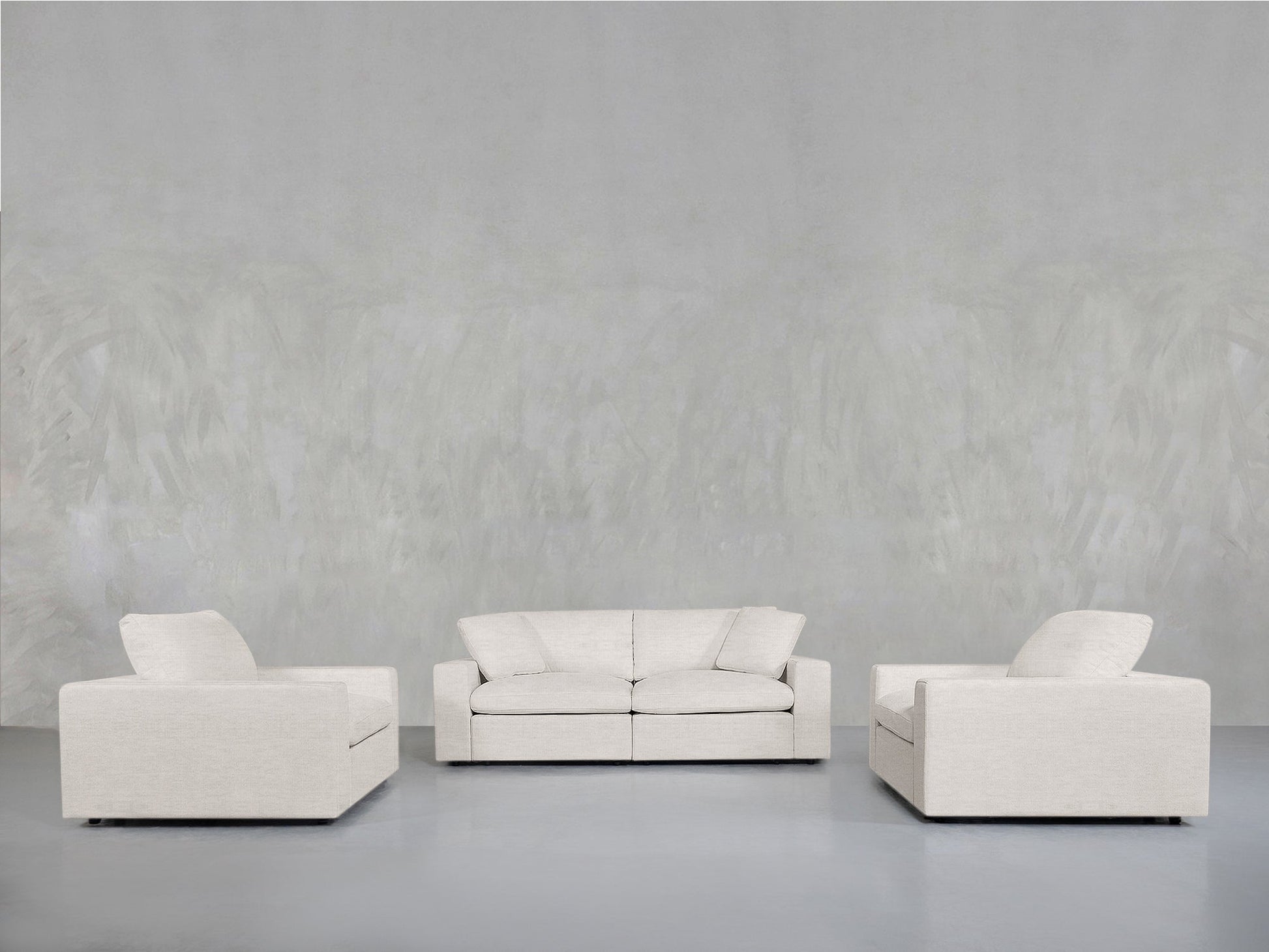 A minimalist living room with a light gray wall, featuring the 2-1-1 Sofa & Armchair Set: a white two-seater sofa in the center and two white armchairs facing it on either side.