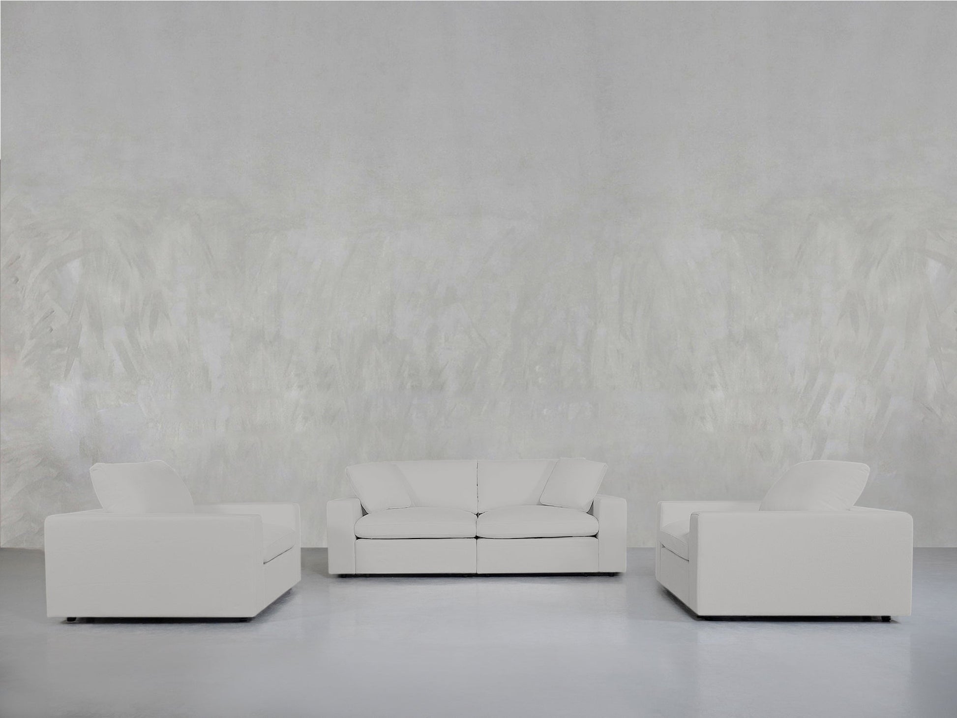 A minimalist living room features the 2-1-1 Sofa & Armchair Set in white, centered and flanked by matching armchairs against a light gray textured wall and smooth, pale flooring.