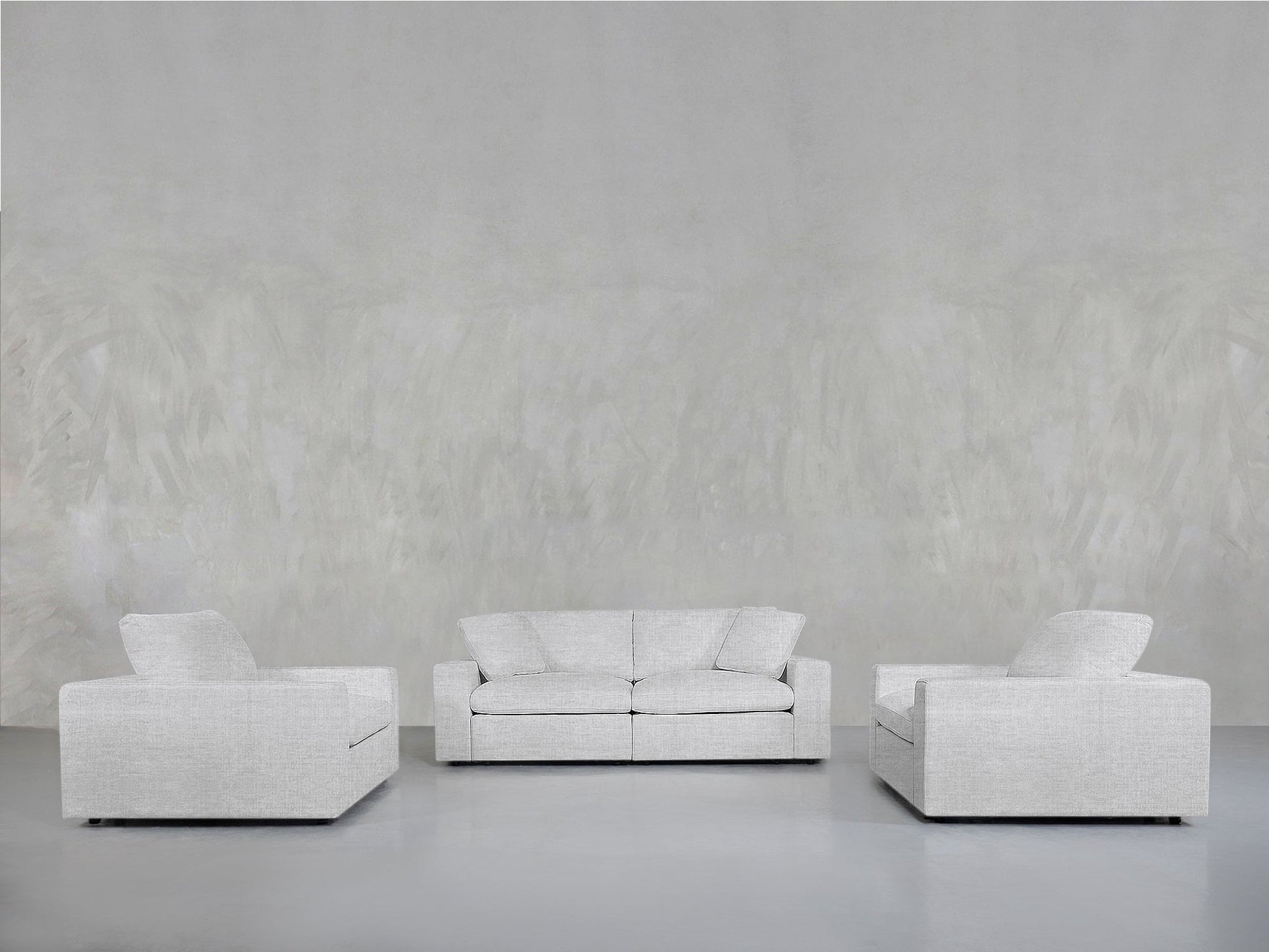 The 2-1-1 Sofa & Armchair Set features a light gray sofa and two matching armchairs, creating a minimalist look in a spacious, neutral room with smooth textured walls and floors.