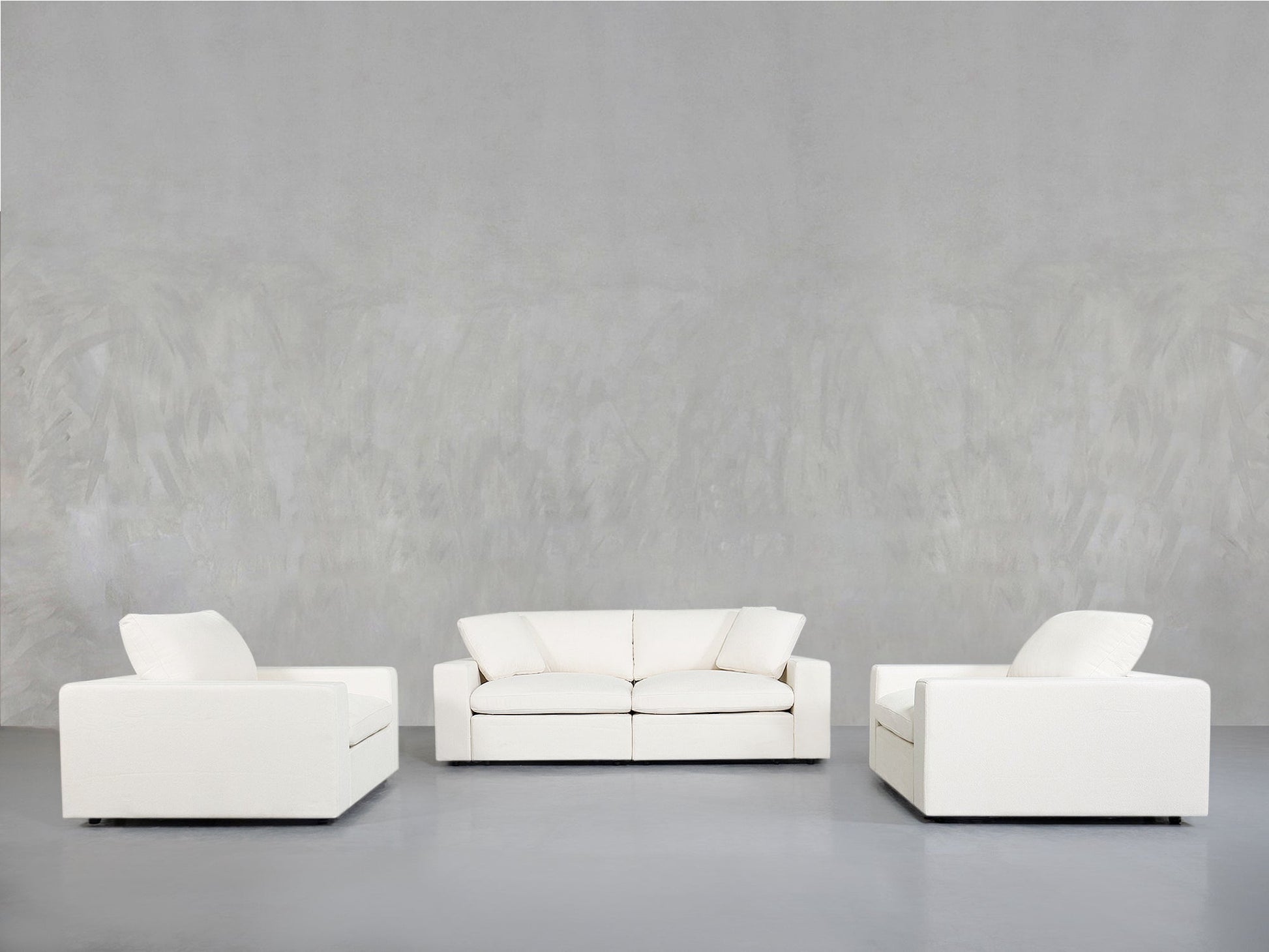 The 2-1-1 Sofa & Armchair Set, featuring a modern two-seater sofa in the center and two single armchairs facing each other, is arranged in a minimalist grey-walled room with a smooth grey floor.