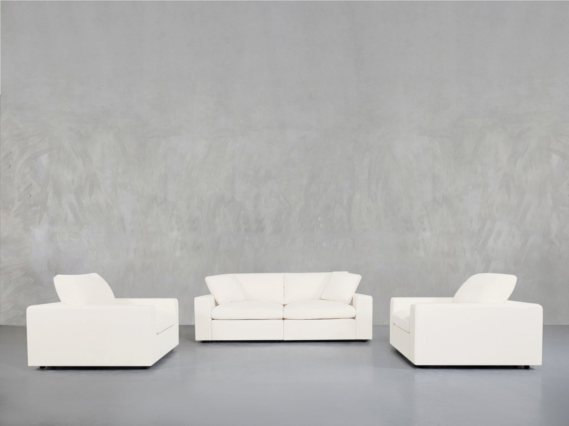 The 2-1-1 Sofa & Armchair Set is displayed in a minimalist room with smooth, light gray walls and floors, featuring a two-seat sofa in the center and single armchairs on each side, all arranged facing forward.