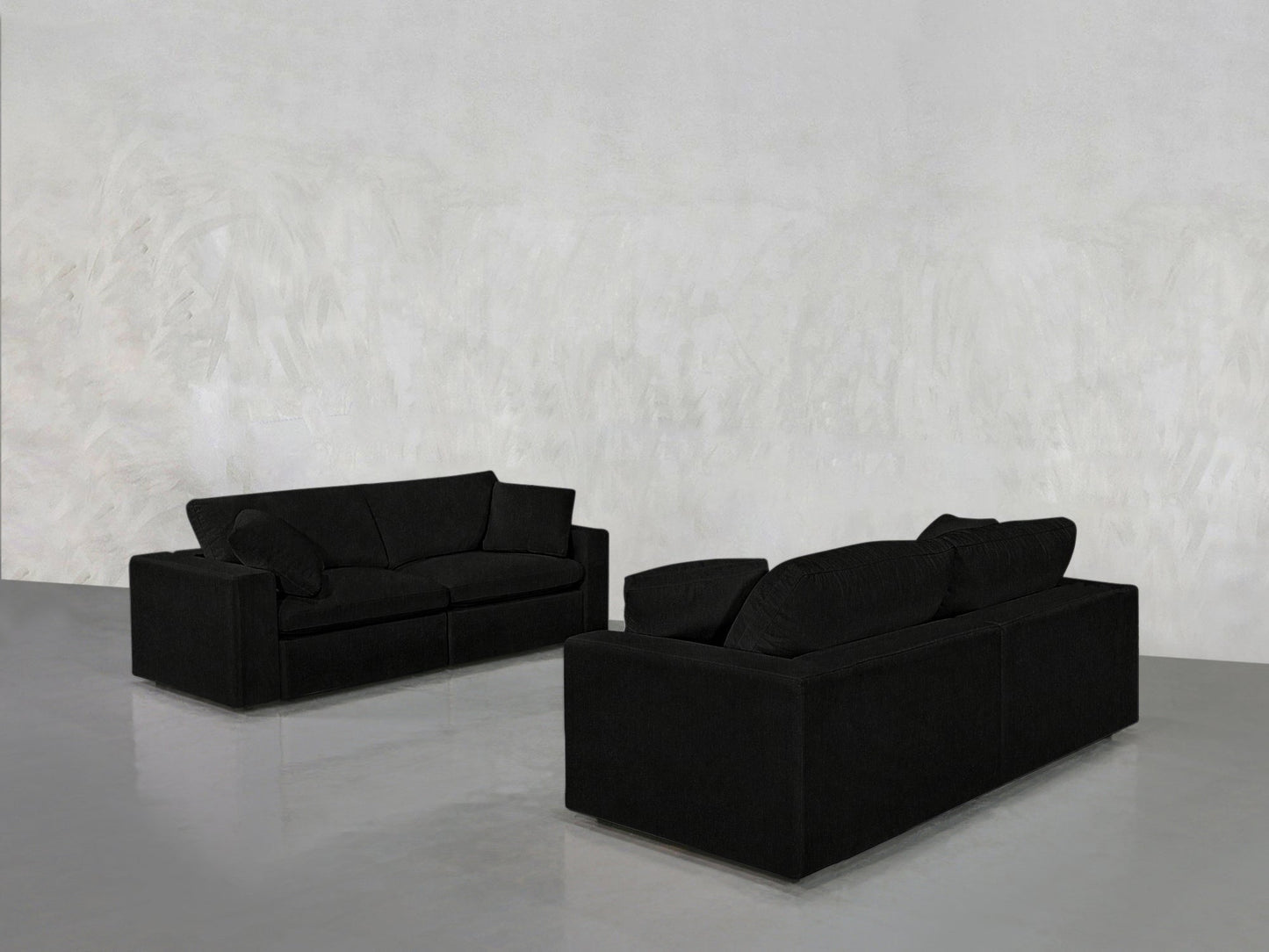 The 2-2 Sofa Set features two modern black sofas arranged opposite each other in a minimalistic room with a light gray textured wall and glossy floor.