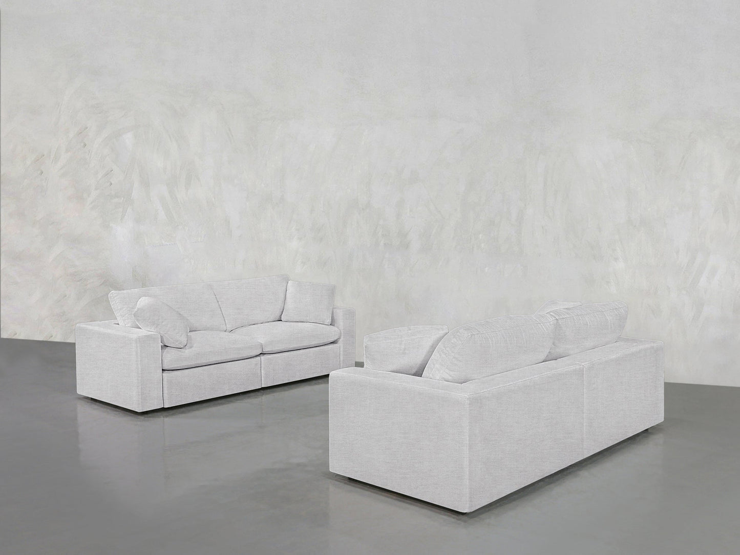 The 2-2 Sofa Set, featuring two modern light gray sofas, is arranged facing each other in a minimalist room with a textured light gray wall and a polished gray floor.
