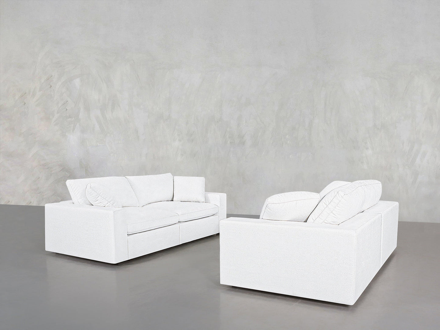 The 2-2 Sofa Set features two modern white couches with cushions, arranged on a smooth gray floor against a textured light gray wall in a minimalist, empty room.