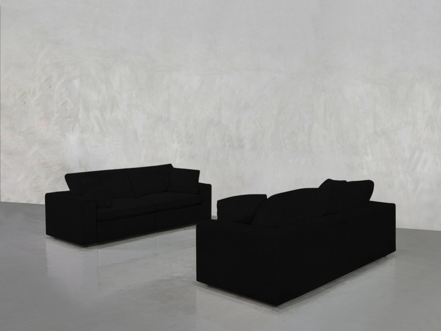 The 2-2 Sofa Set, featuring two modern black sofas, is arranged face-to-face in a minimalist room with textured light gray walls and a shiny gray floor for a simple, uncluttered look.