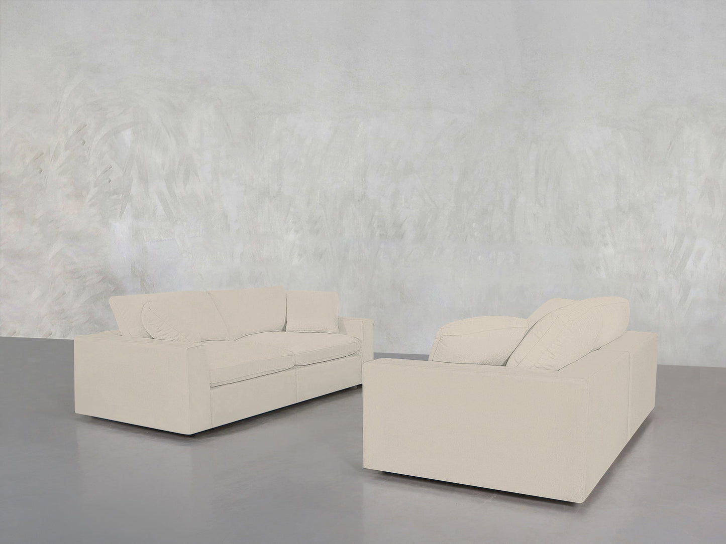 Two cream-colored 2-2 Sofa Set pieces are arranged in an L-shape on a gray floor with a light textured wall behind them, creating a minimalistic and modern atmosphere.
