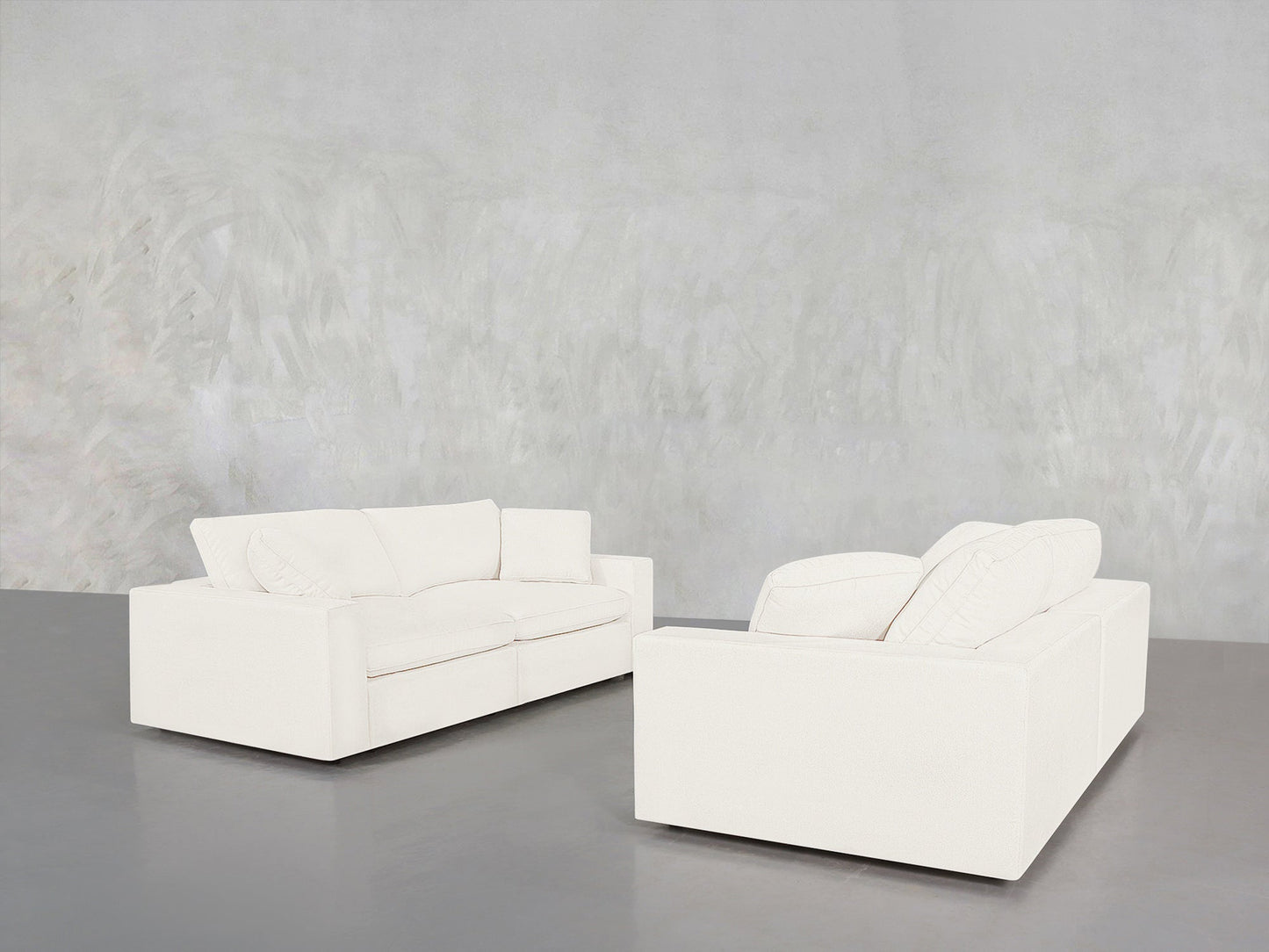 The 2-2 Sofa Set, featuring two modern white sofas with cushions, is arranged facing each other in a minimalist room with a textured light gray wall and a polished gray floor.