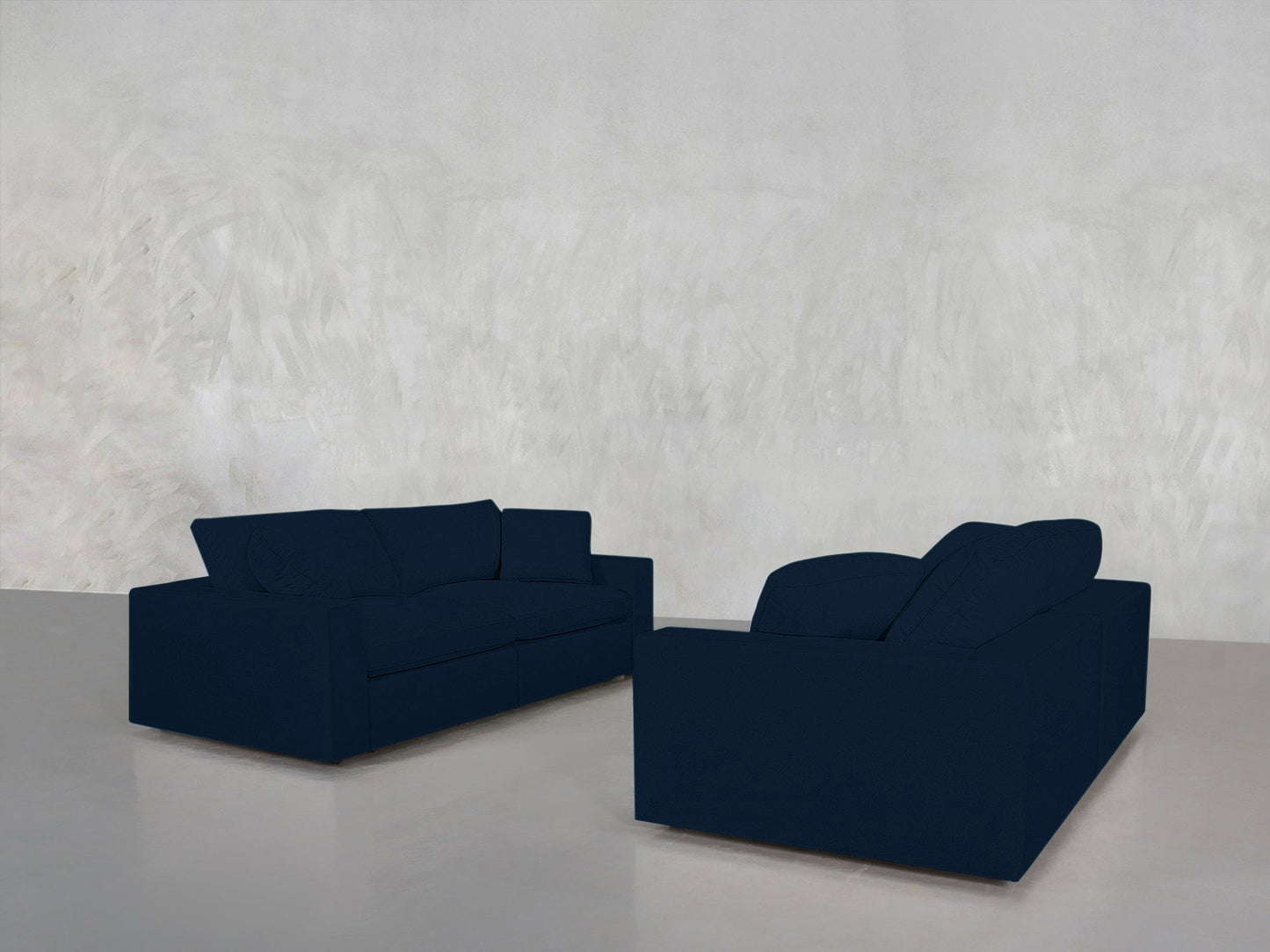 The 2-2 Sofa Set in dark blue is arranged facing each other in a minimalistic room with a light gray textured wall and a smooth, light floor, creating an open and uncluttered space.