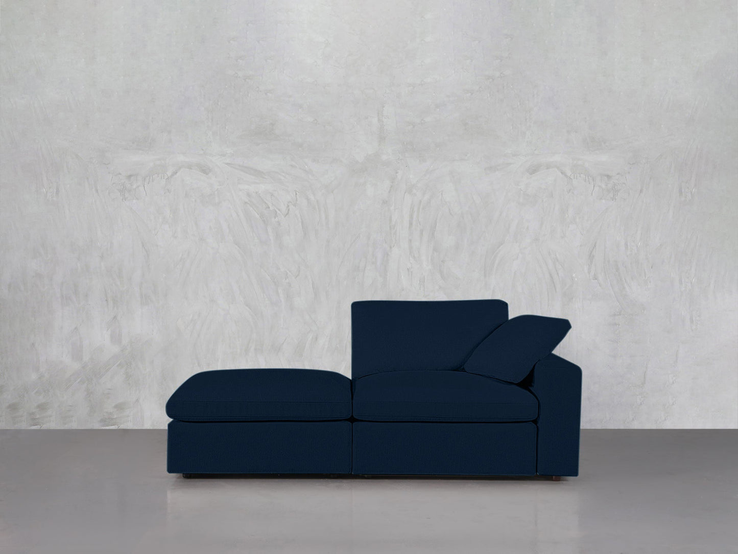 A 2-Seat Modular Lounger Loveseat in modern dark blue with chaise lounge and back cushions sits against a light textured gray wall on a polished gray floor.