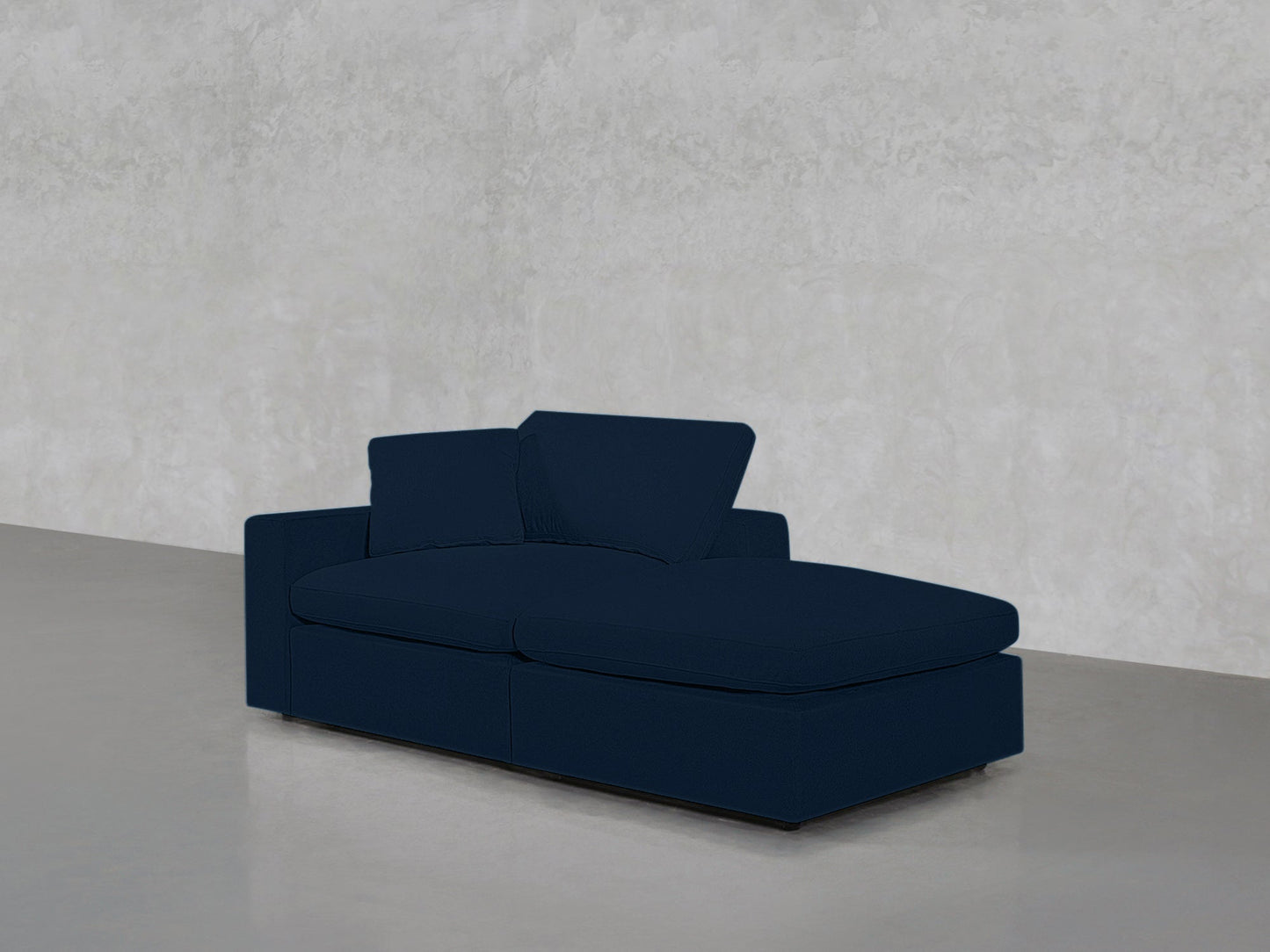 A sleek 2-Seat Modular Lounger Loveseat in dark blue with a backrest and armrest sits on a smooth light gray floor, set against a textured pale gray wall.