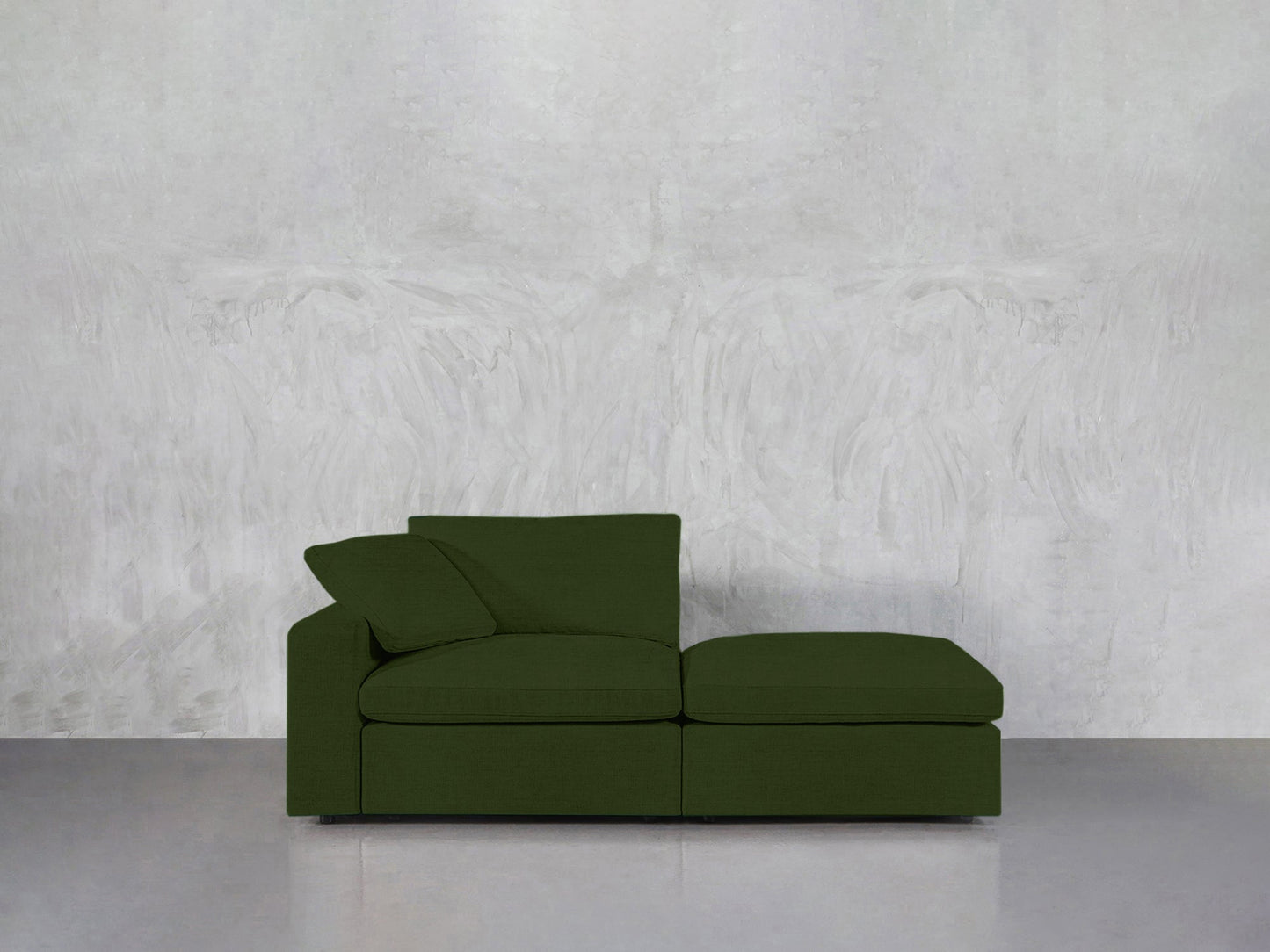A sleek green 2-Seat Modular Lounger Loveseat with a matching cushion is placed against a textured light gray wall on a smooth gray floor.