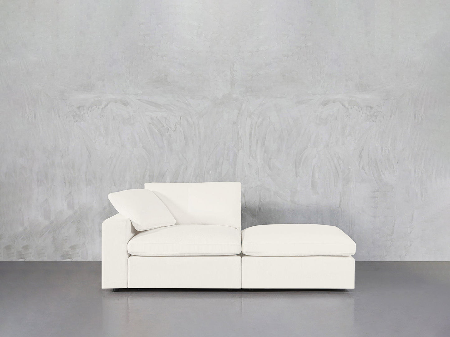 A 2-Seat Modular Lounger Loveseat in modern white with a single cushion and pillow is set against a light gray textured wall atop a smooth gray floor.
