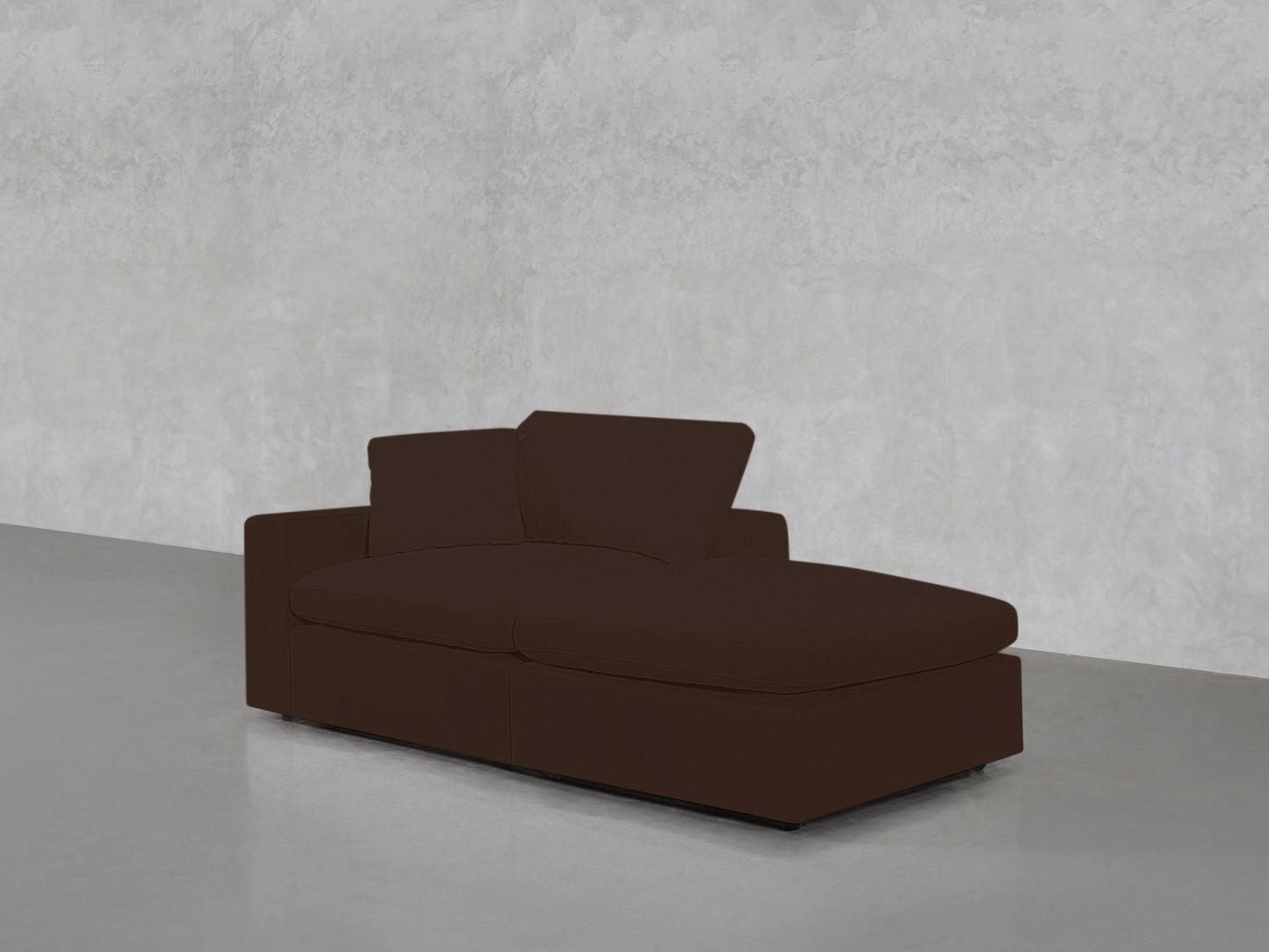 The 2-Seat Modular Lounger Loveseat in brown features a low backrest and armrest, positioned on a smooth light gray floor against a textured light gray wall.