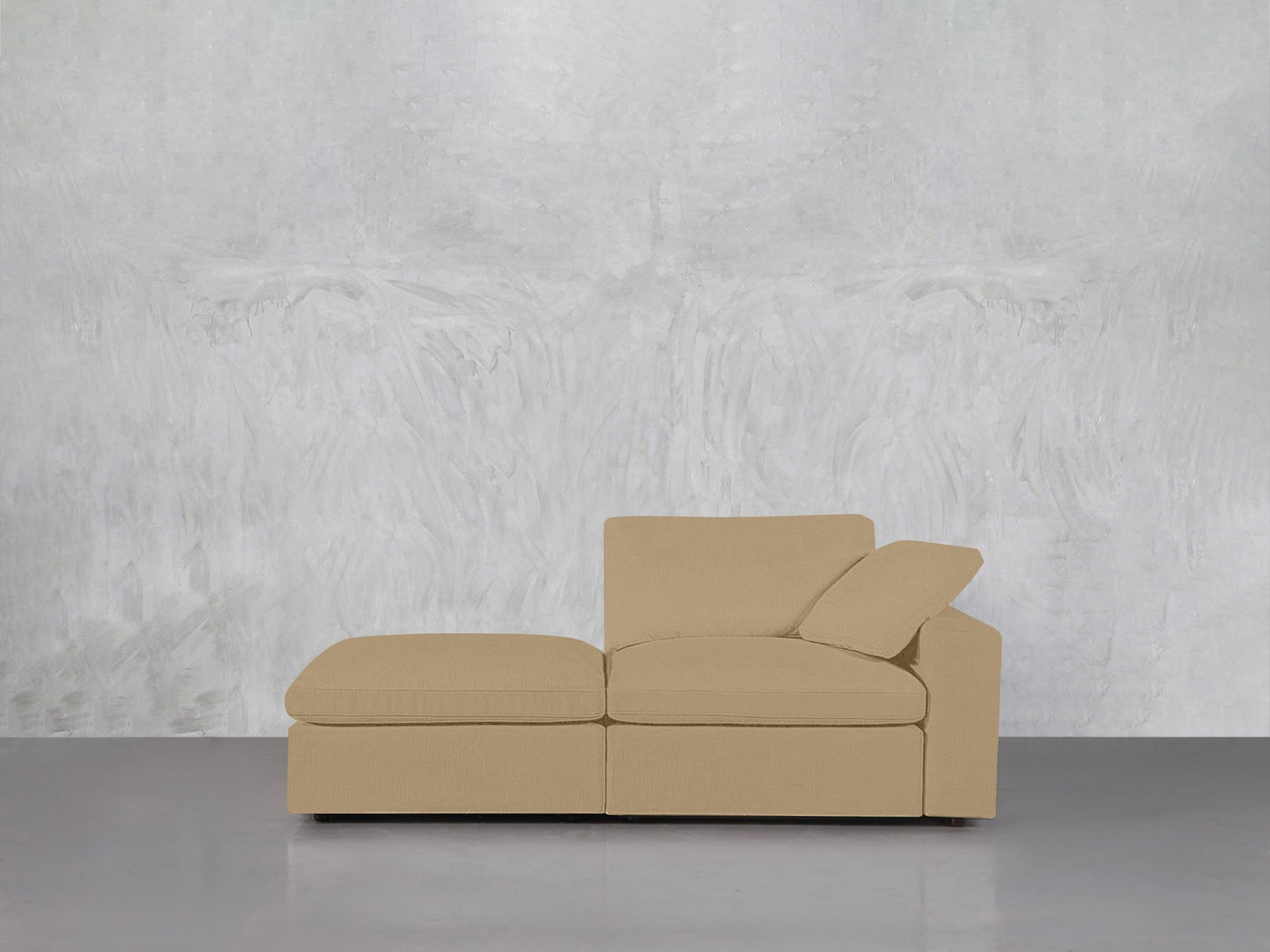 A 2-Seat Modular Lounger Loveseat with chaise and one armrest sits on a smooth gray floor before a light gray textured wall.