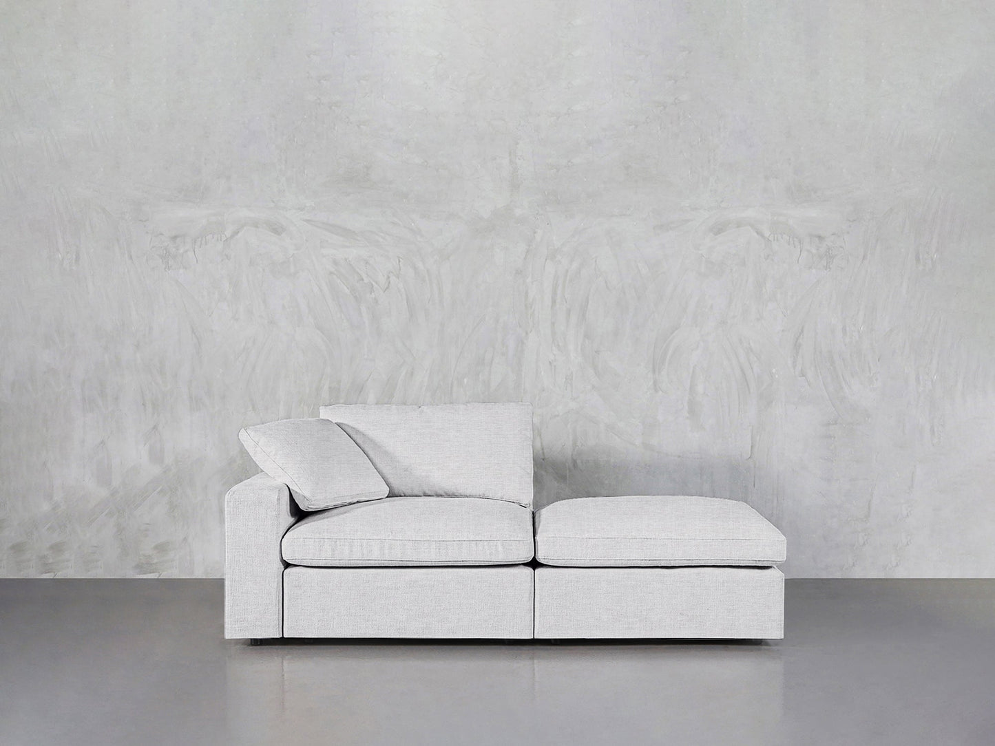A modern 2-Seat Modular Lounger Loveseat in light gray upholstery with two seat and back cushions sits against a textured, light gray wall on a smooth, gray floor.