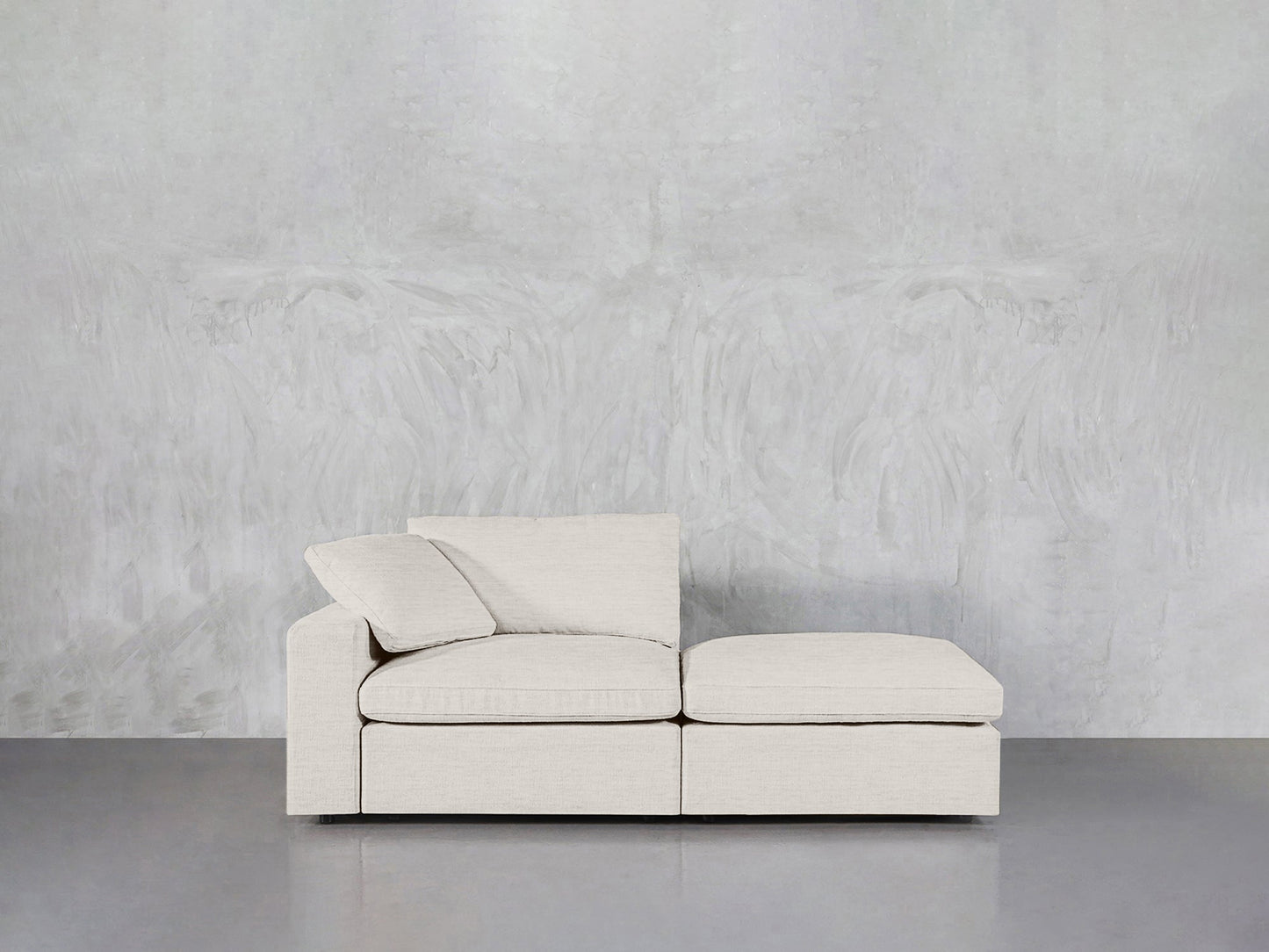 A modern, light beige 2-Seat Modular Lounger Loveseat with two cushions sits against a textured pale gray wall on a smooth, reflective gray floor.