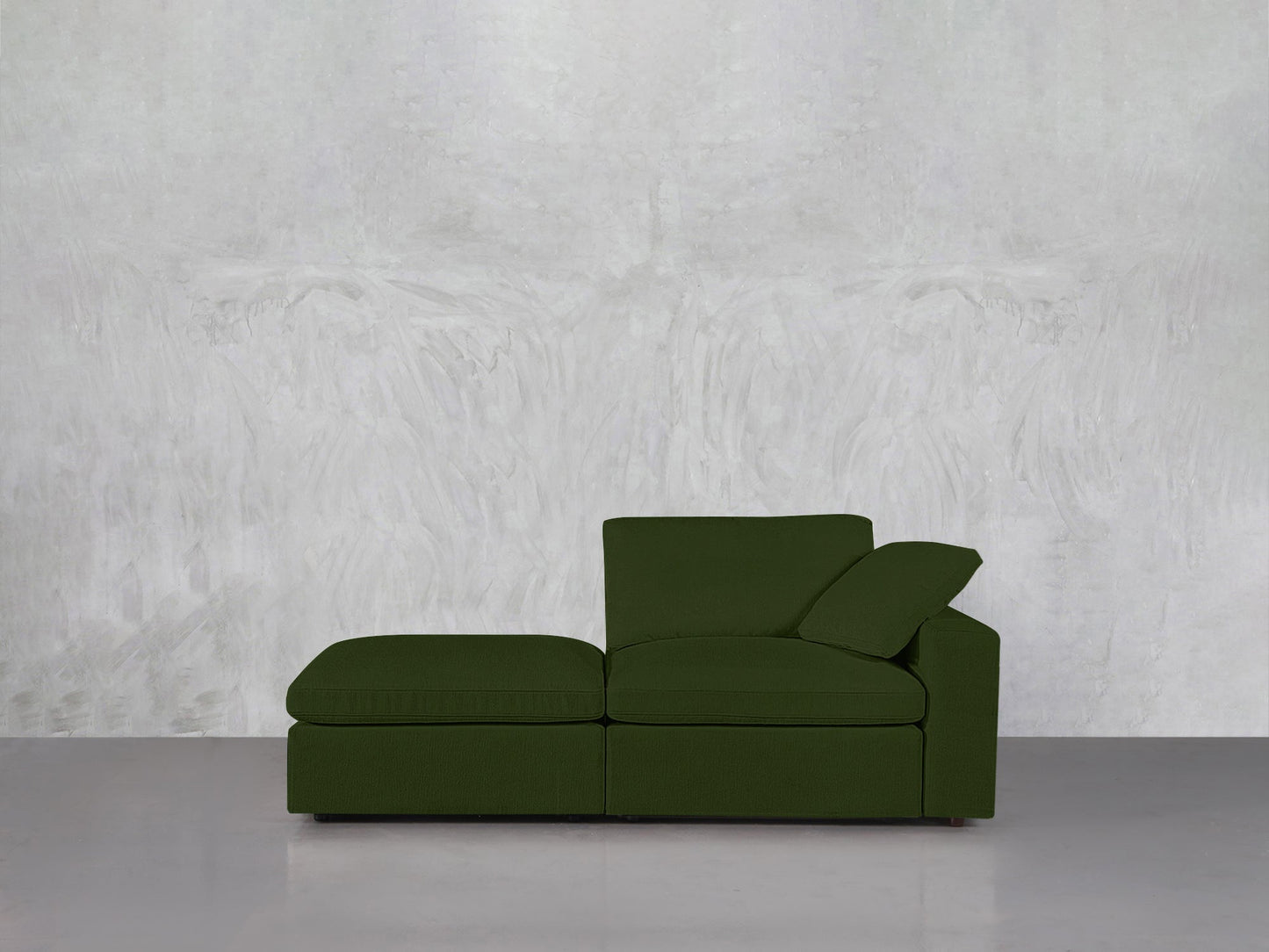 The 2-Seat Modular Lounger Loveseat in green, featuring a chaise lounge, single back cushion, and angled armrest, is set on a glossy gray floor with a textured pale gray wall as the backdrop.