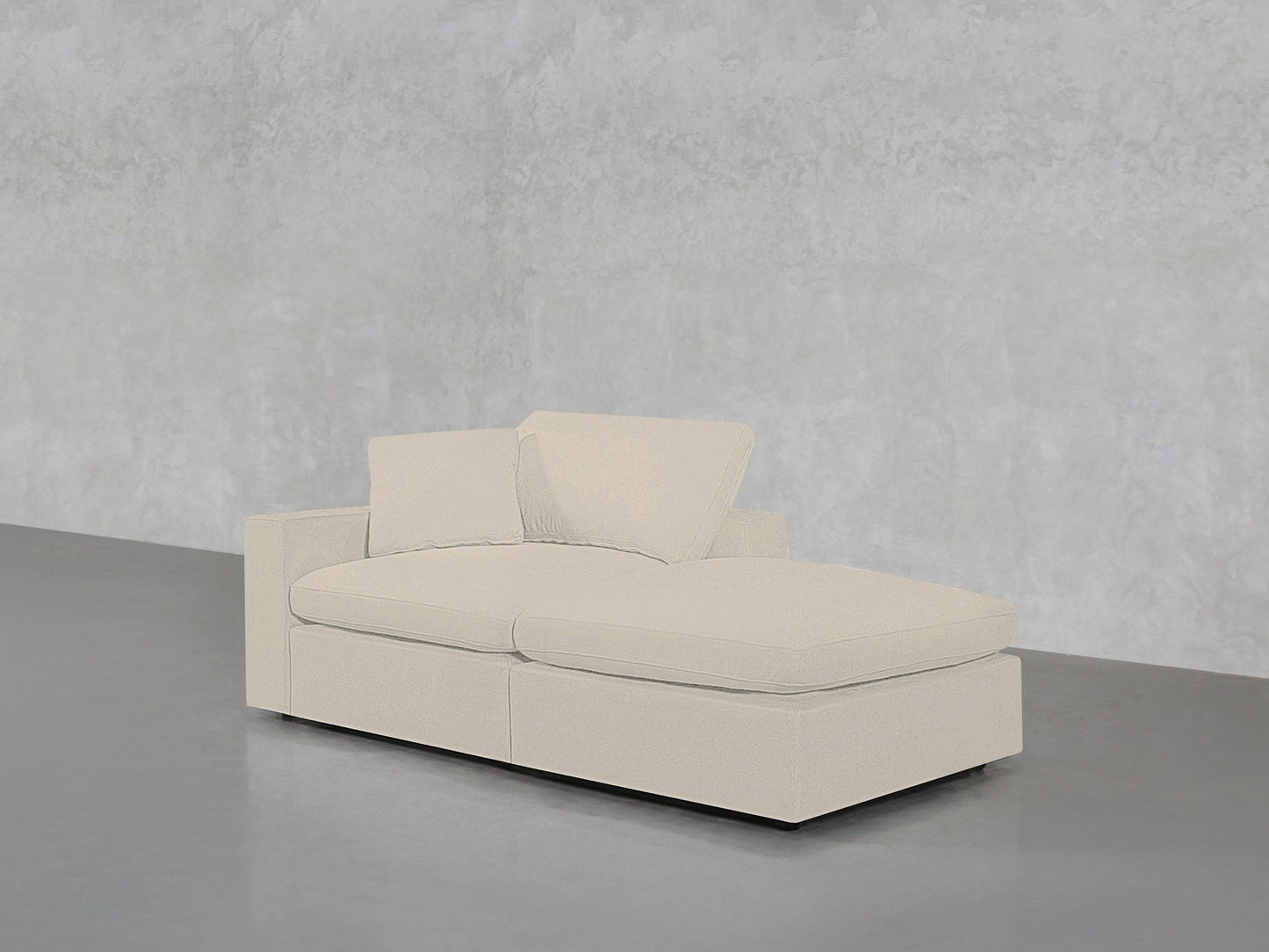 The 2-Seat Modular Lounger Loveseat in light beige, featuring two back cushions, is placed on a smooth gray floor against a textured light gray wall.