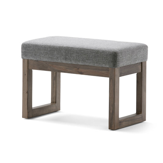 The Milltown Upholstered Ottoman Bench features a small, rectangular cushioned gray fabric seat and a simple wooden frame with square legs.