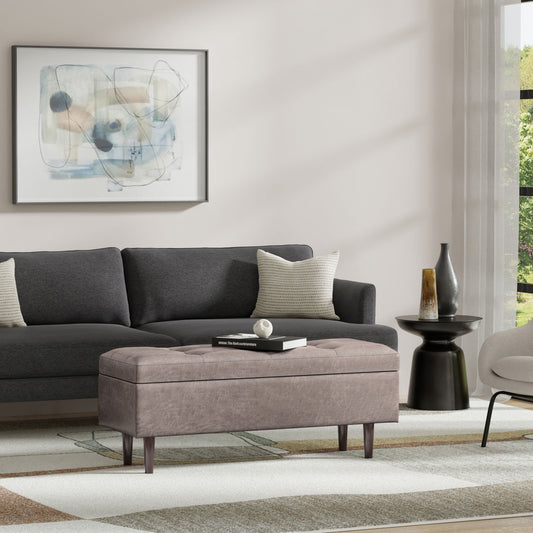 A modern living room with a dark gray sofa, the Shay Large Square Coffee Table Storage Ottoman in mid-century style, a round black side table with decor, abstract wall art, and sunlight streaming through sheer curtains.