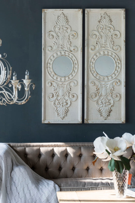 A tufted beige sofa with a gray throw sits beneath two Large Wooden Wall Art Panels With Distressed Round Mirror Accents (Set of 2) - White, in a cozy, elegant room featuring dark walls, a chandelier, and a vase of white flowers.