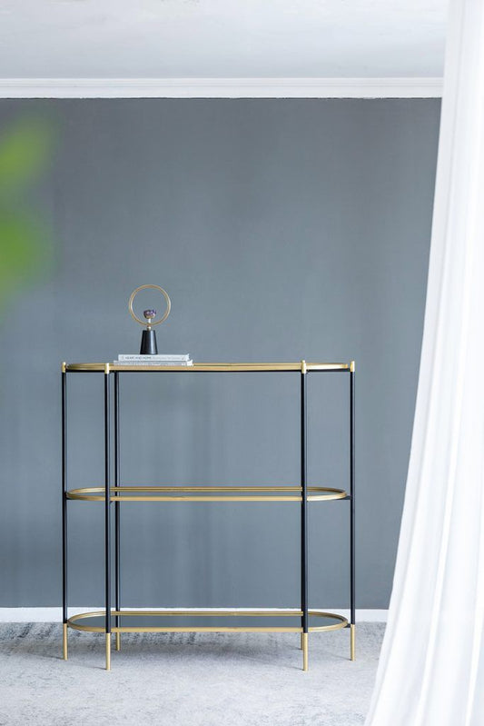 The 3 Tier Metal Console Table, Mirrored Shelf - Golden Black stands against a gray wall, displaying a small decorative object and books on its top shelf. White curtains partially frame the right side of the scene.