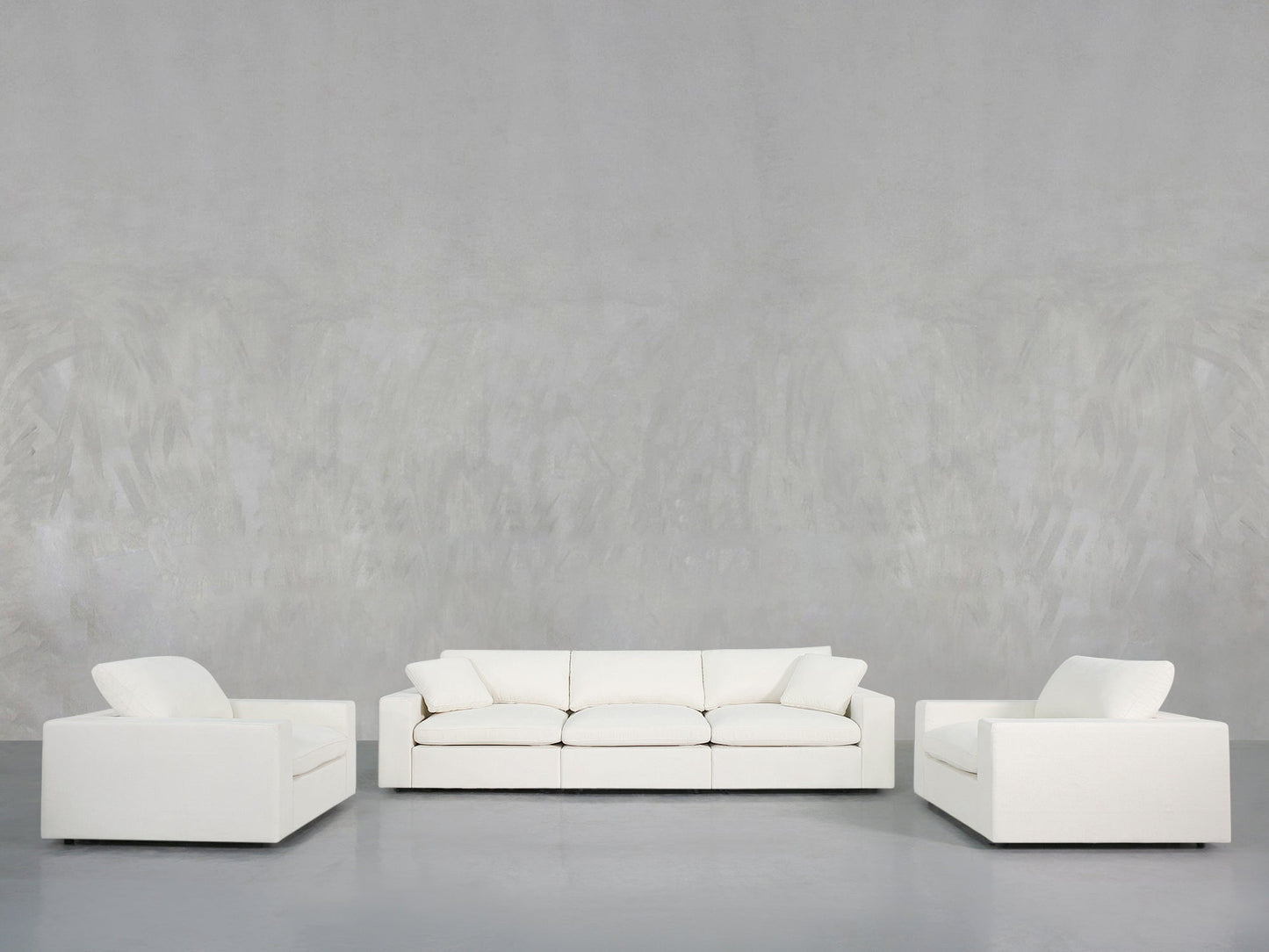 The 3-1-1 Sofa & Armchair Set includes a white sofa and two matching armchairs, arranged on a gray floor with a textured light gray wall backdrop for a minimalist look.