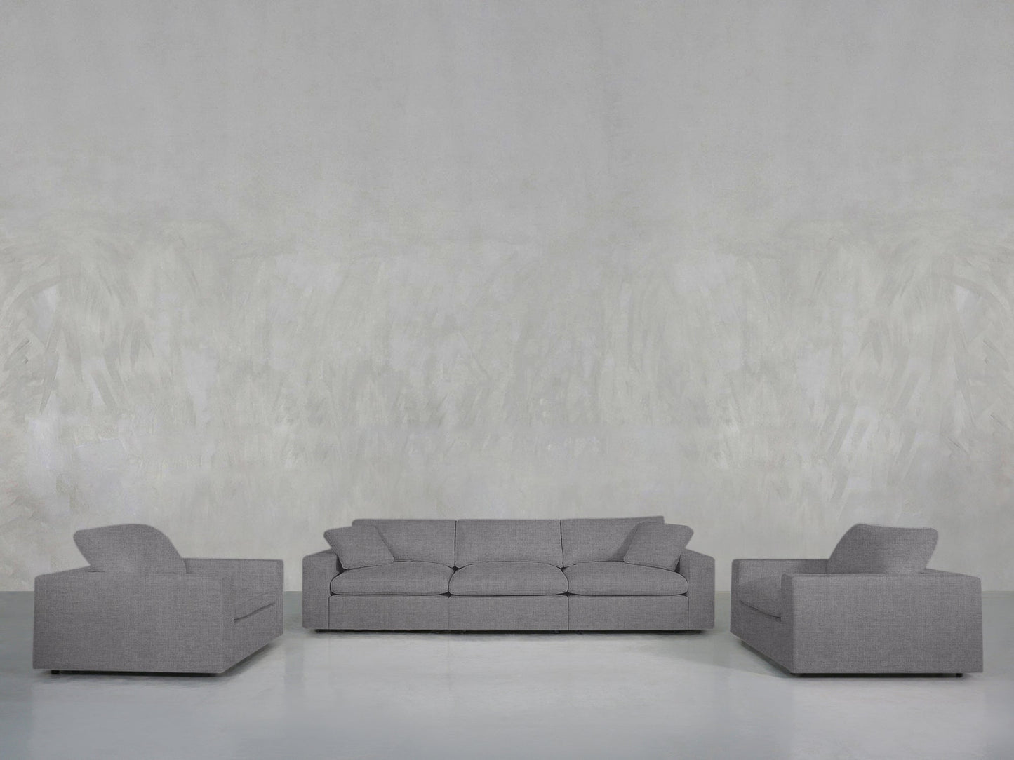 The 3-1-1 Sofa & Armchair Set features a gray sofa and two matching armchairs, arranged on a light floor against a textured light gray wall for a minimalist living room look.