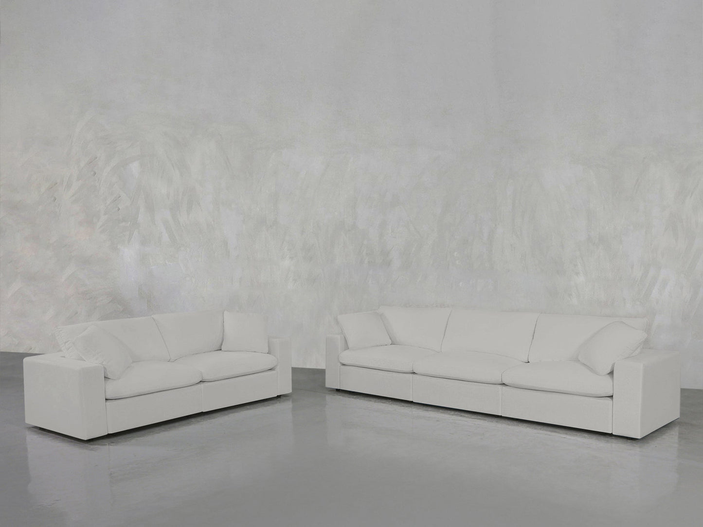 The 3-2 Sofa Set, featuring modern white sofas with clean lines, is arranged in a minimalistic room with a textured light gray wall and a shiny gray floor.