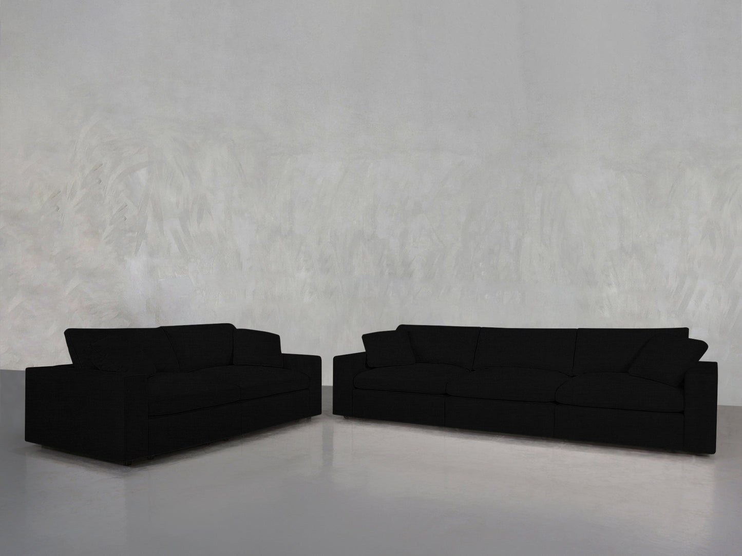 The 3-2 Sofa Set is arranged in an L-shape against a light grey textured wall on a polished grey floor, creating a minimalist, modern setting.