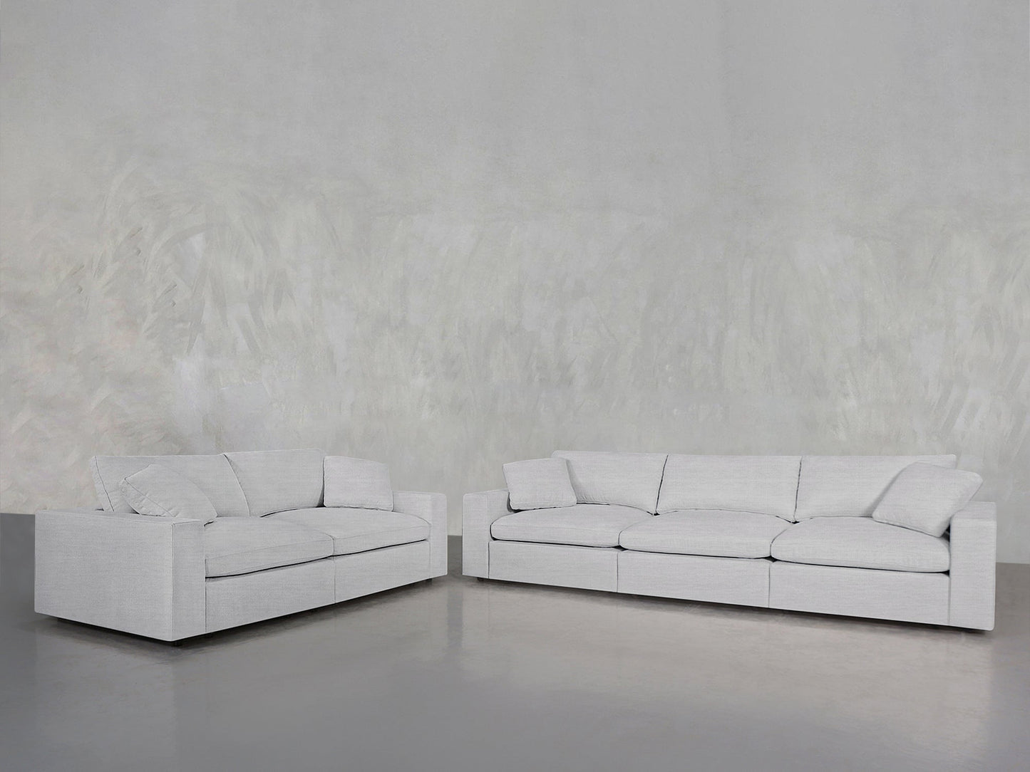 A 3-2 Sofa Set in modern light gray with clean lines and plush cushions is arranged in an L-shape against a minimalist, textured gray wall and polished gray floor.