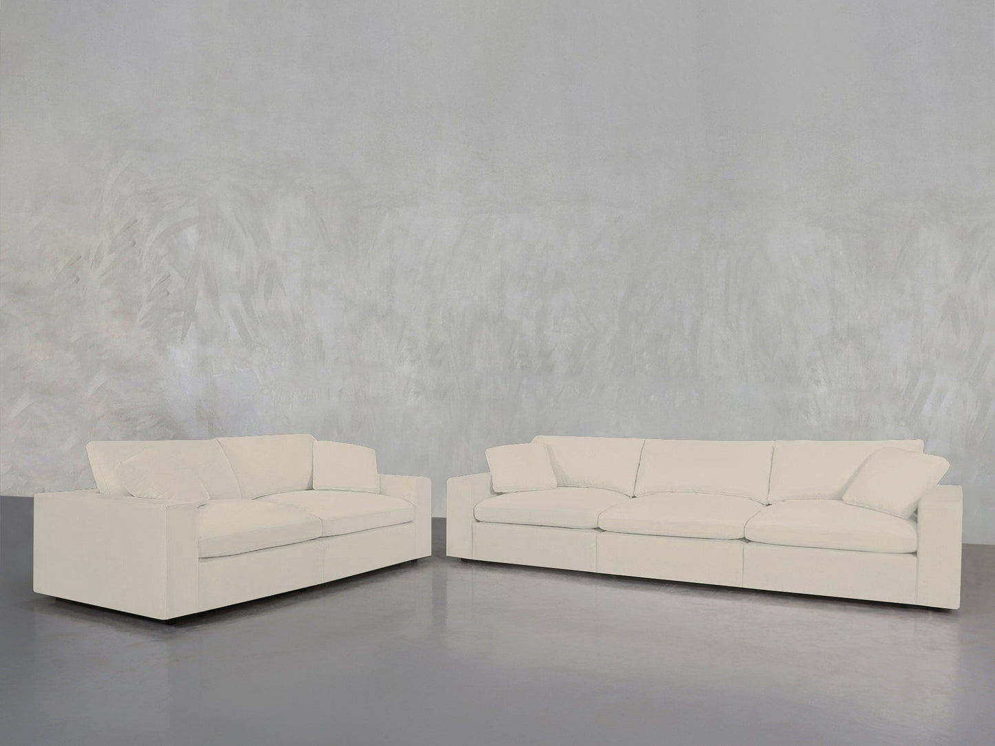 A minimalistic, uncluttered space features the 3-2 Sofa Set—two modern off-white sofas with clean lines—arranged on a polished concrete floor against a light gray textured wall.
