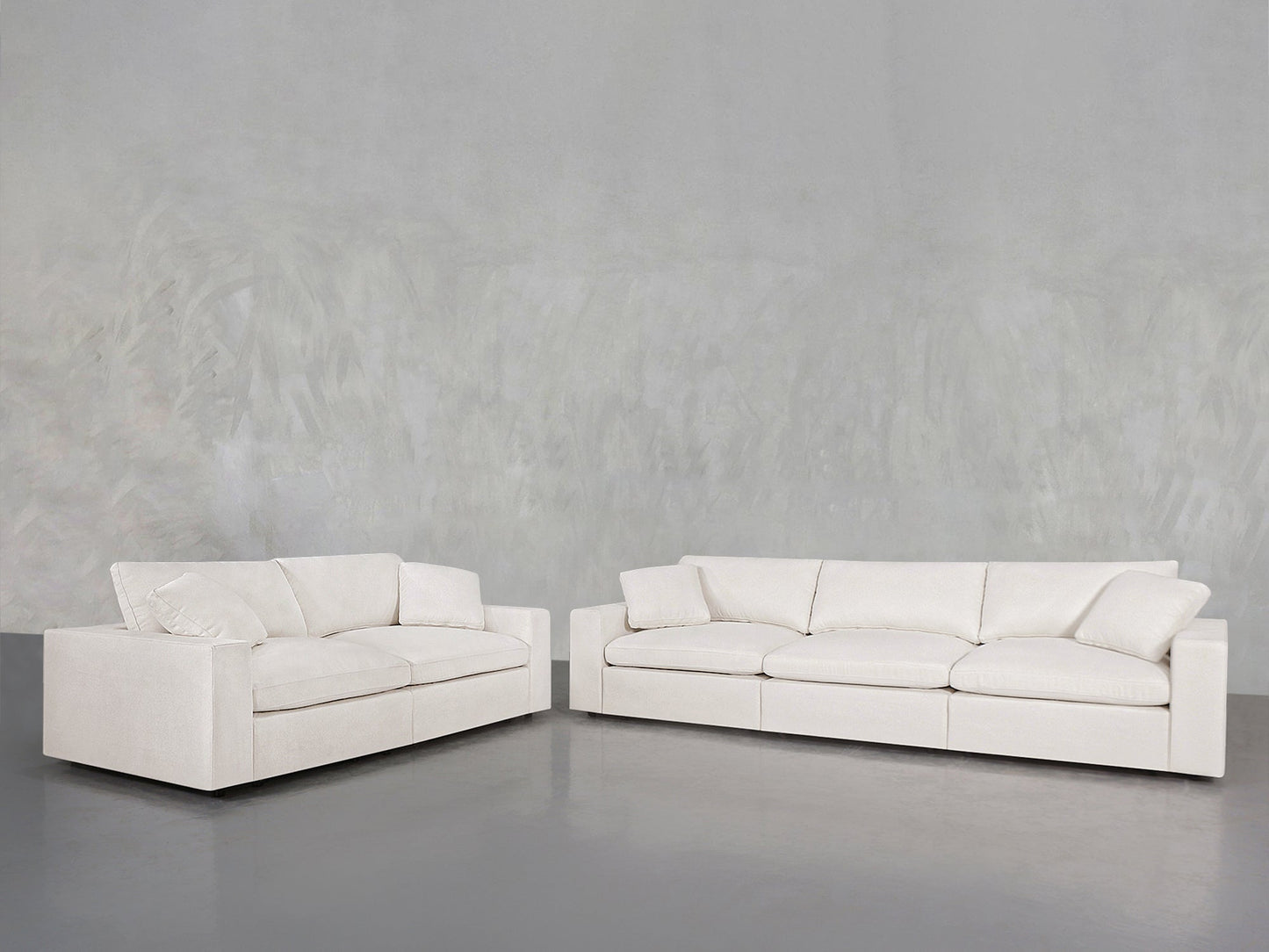 The 3-2 Sofa Set, featuring modern white upholstery with square arms and plush cushions, is arranged in an L-shape against a light gray textured wall and a smooth gray floor.